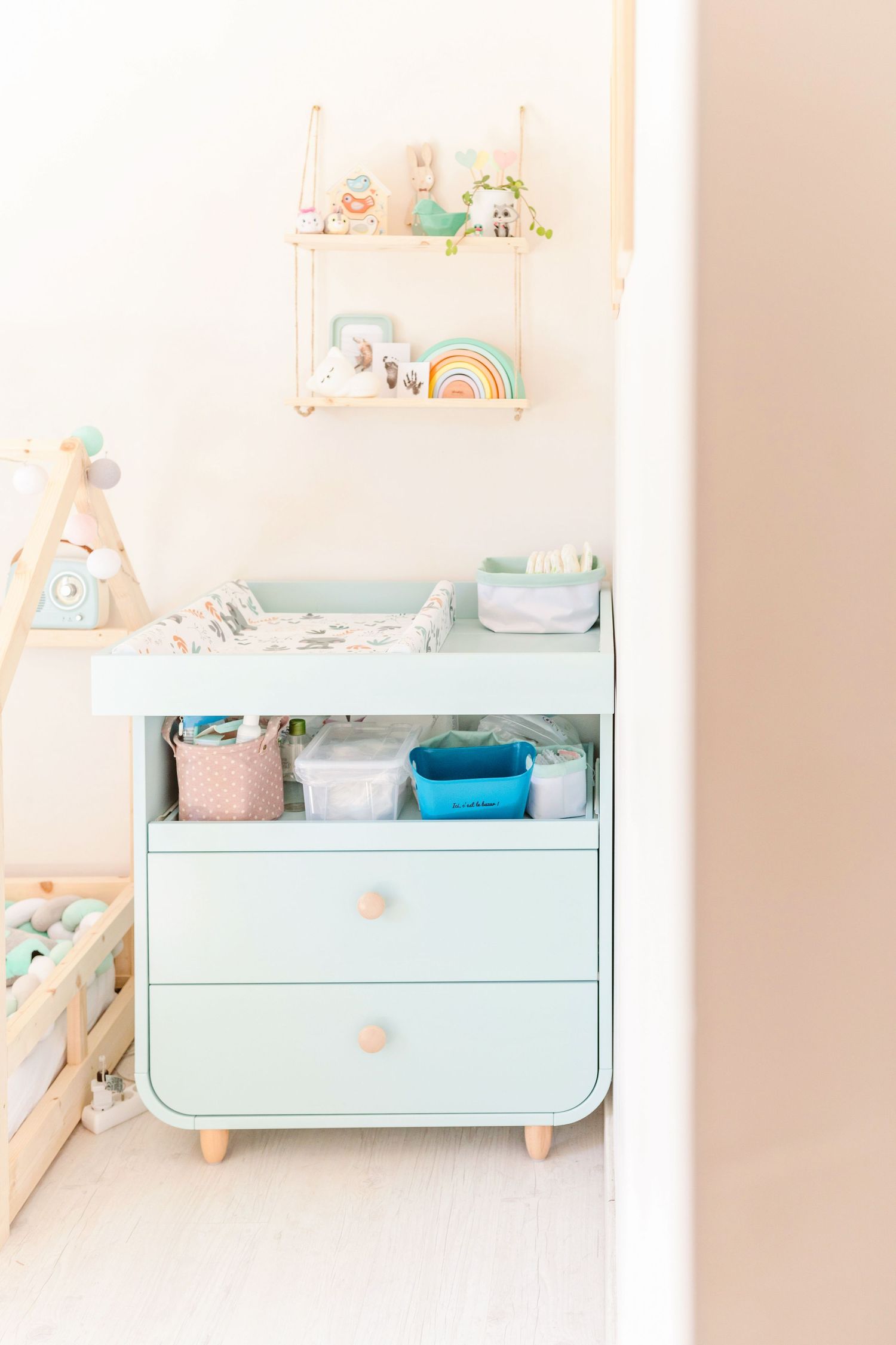 Mint green nursery dresser with shelving displaying various baby items and decorations.