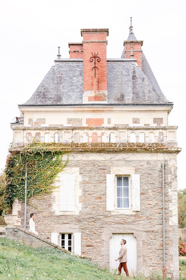 Historic French chateau with stone walls, red chimneys and slate roof against cloudy sky.