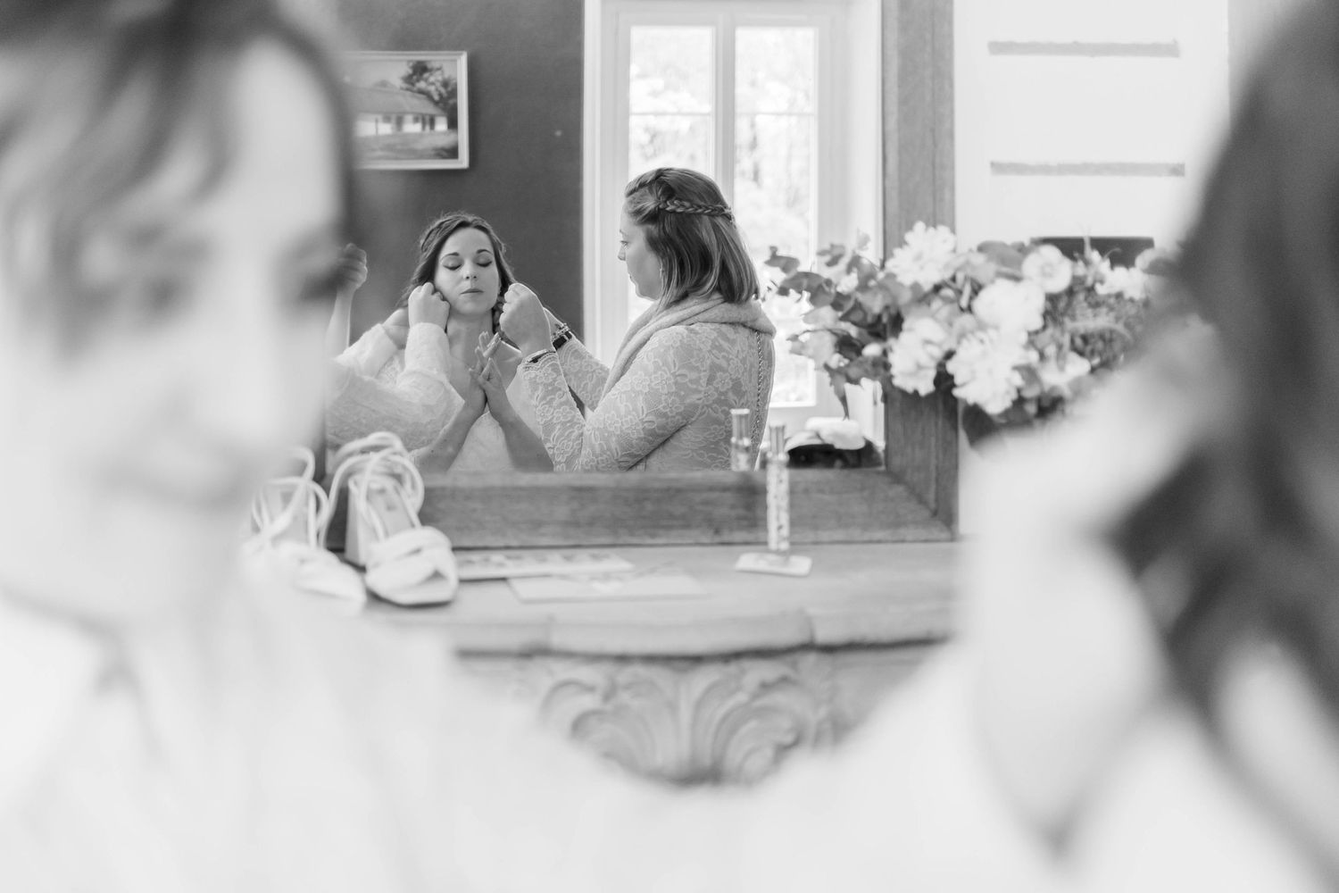 Black and white reflection of people getting ready in mirror with flowers in foreground.