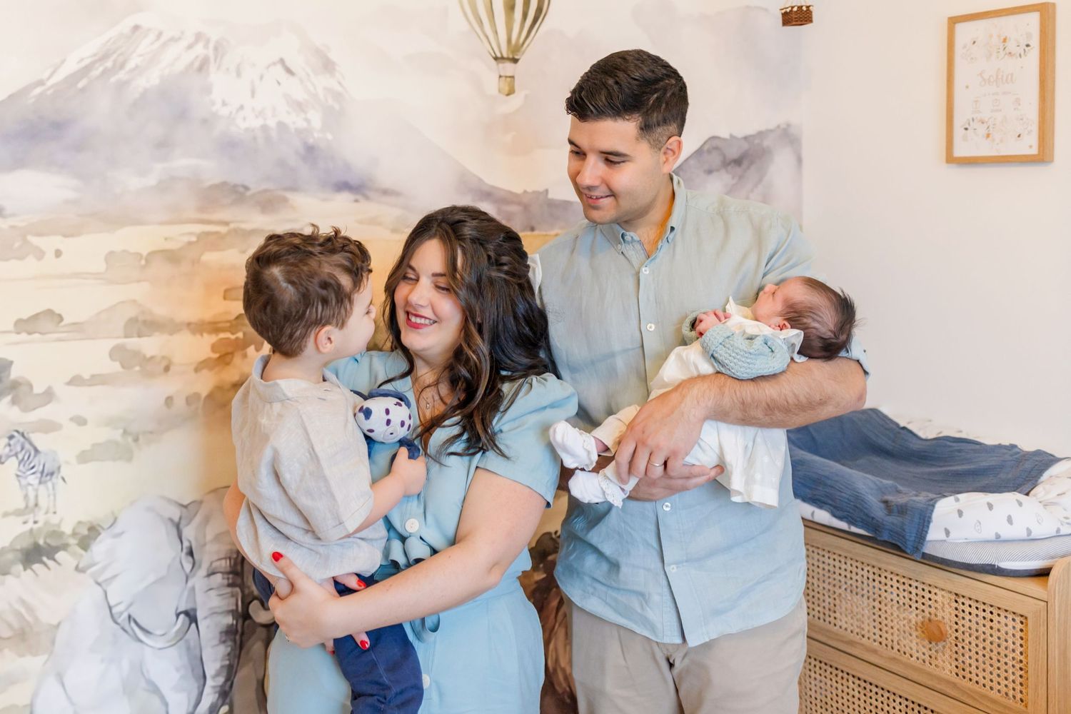 Happy family gathering in nursery with mountain mural and warm lighting.