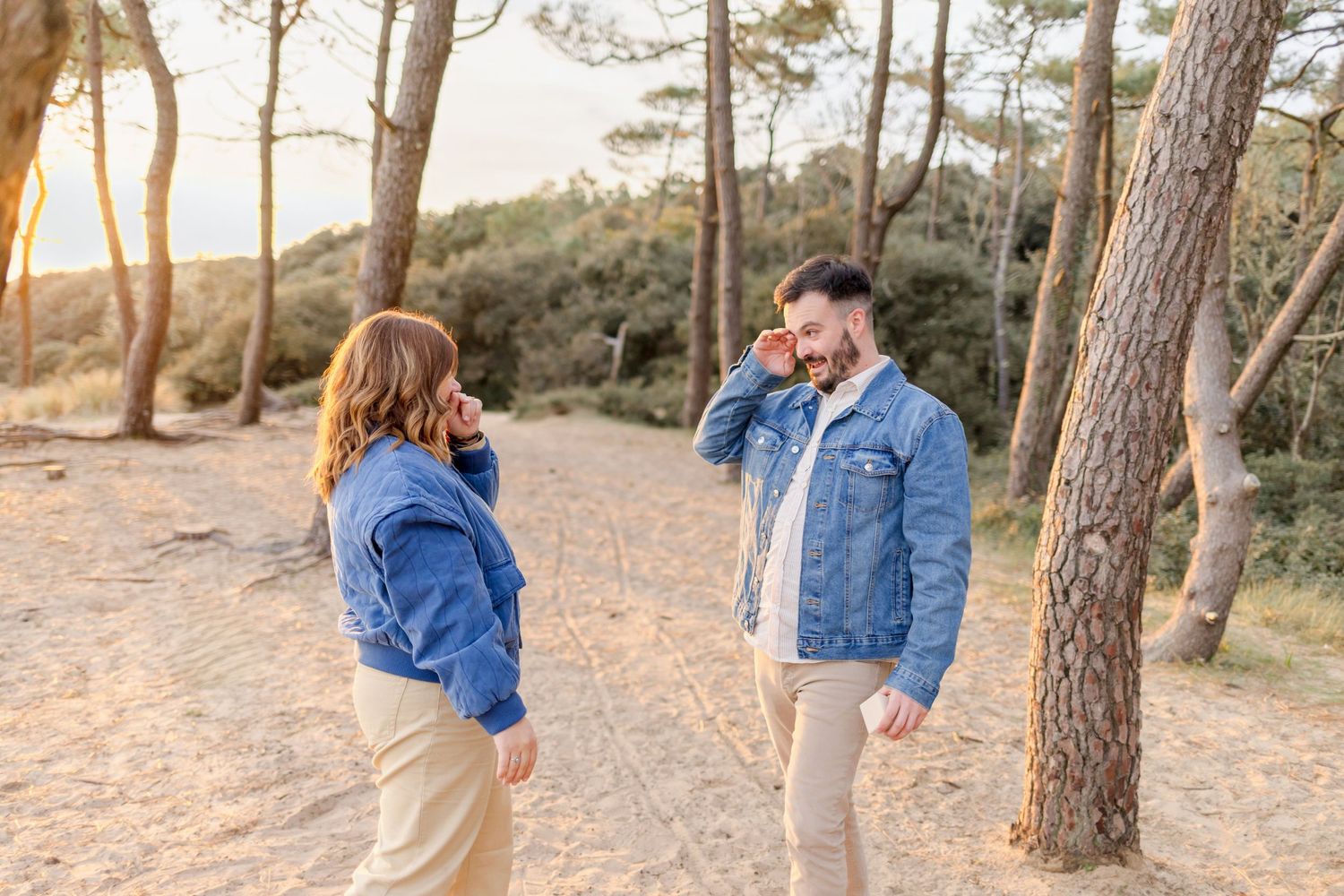 A couple shares a tender moment while standing among pine trees at sunset.