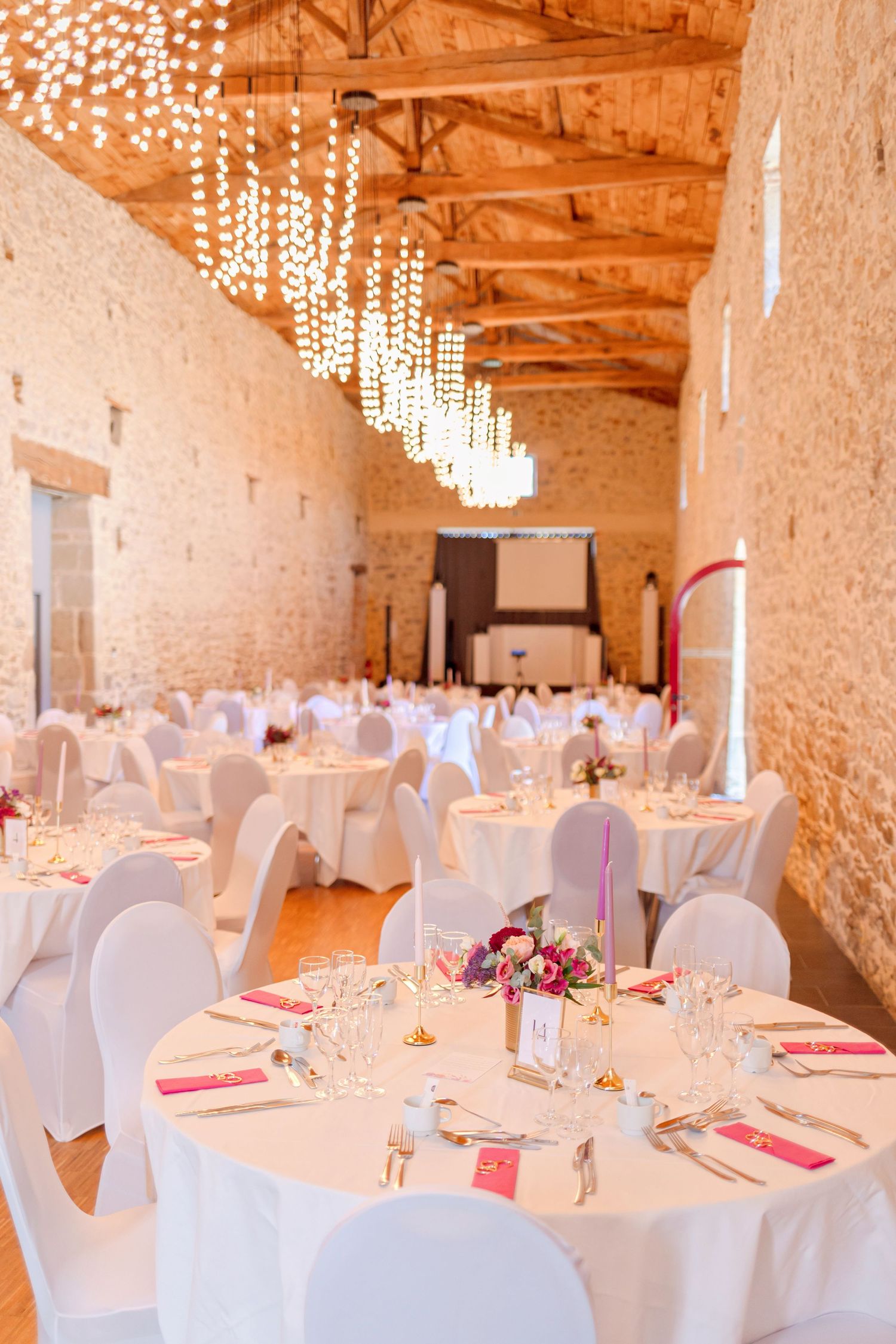 Elegant wedding reception hall with hanging crystal lights and white-covered round tables.