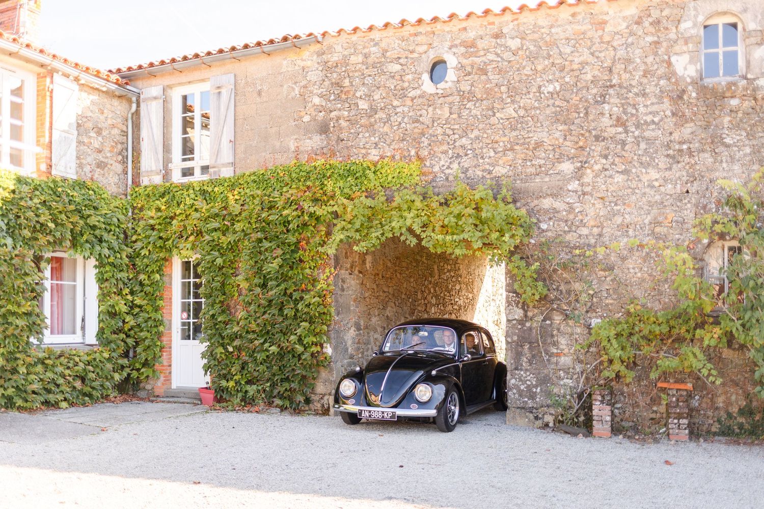 A vintage black Volkswagen Beetle parked under an ivy-covered stone archway.