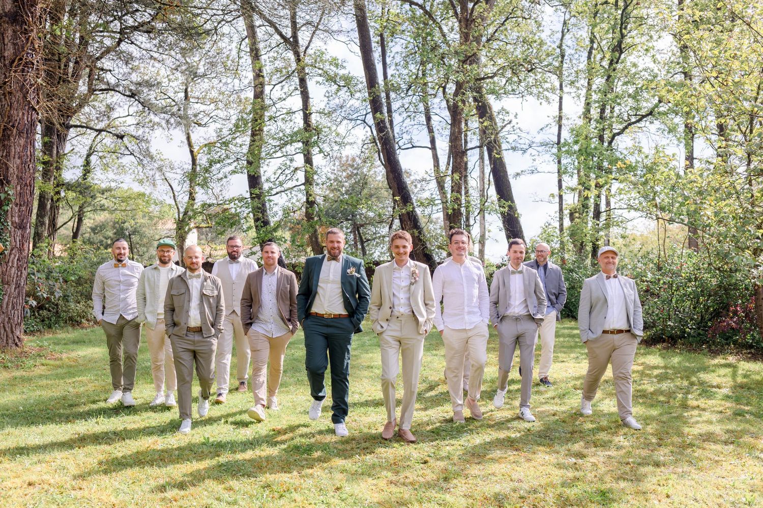 Groomsmen in light colored suits walking together through a wooded outdoor setting.