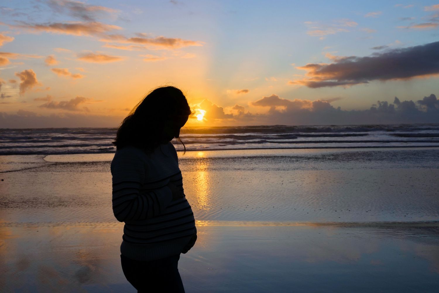 Silhouette of an expectant mother against a golden beach sunset.