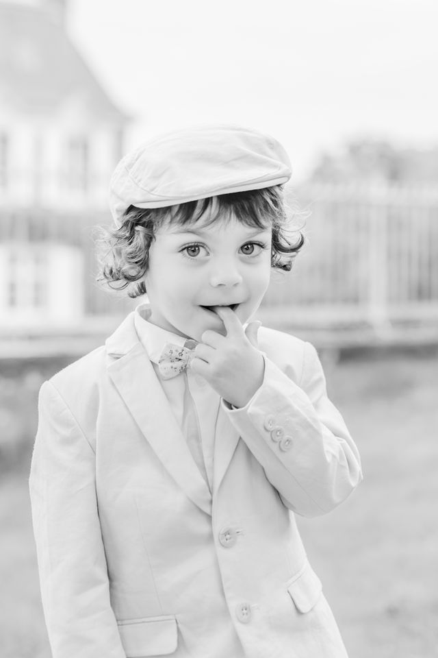 Young child in white suit and cap poses playfully outdoors.