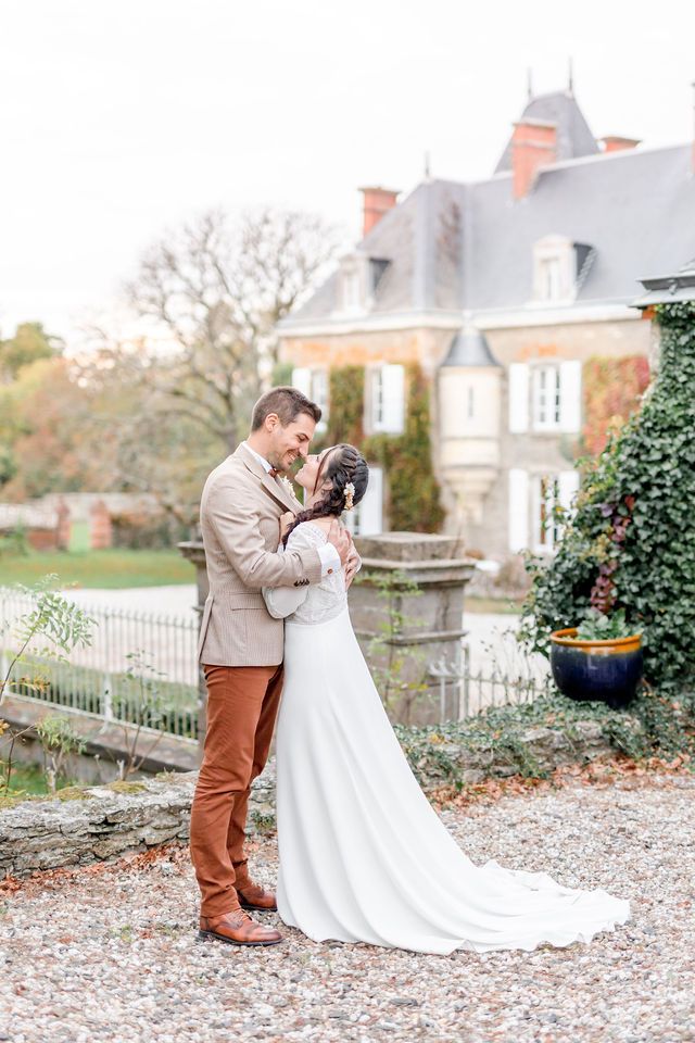 Wedding couple embracing in front of a grand French chateau with rustic garden details.