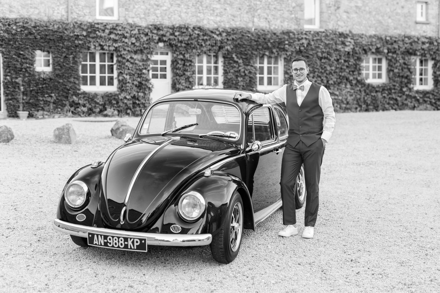 Vintage black and white photo showing person standing beside classic Volkswagen Beetle.