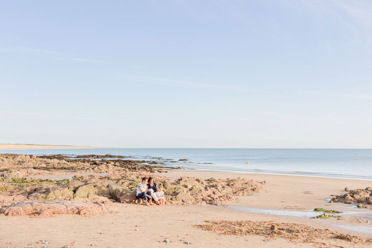 A serene beach landscape with distant figures and rocky outcrops along the shore.