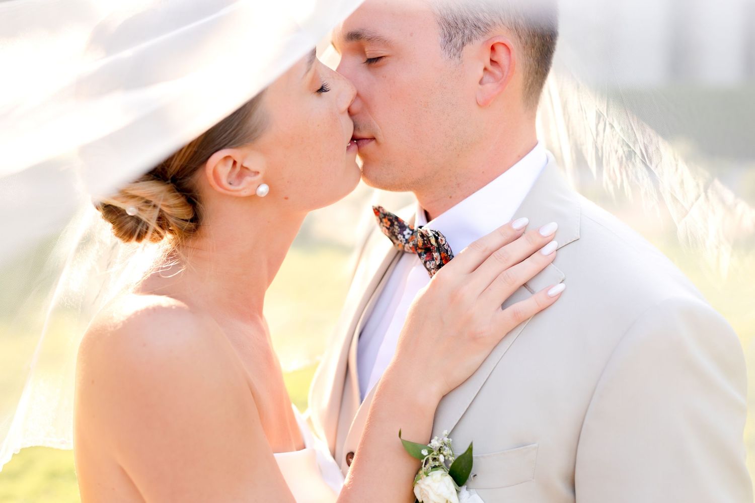 A romantic wedding moment captured in soft sunlight with the bride's veil floating delicately.