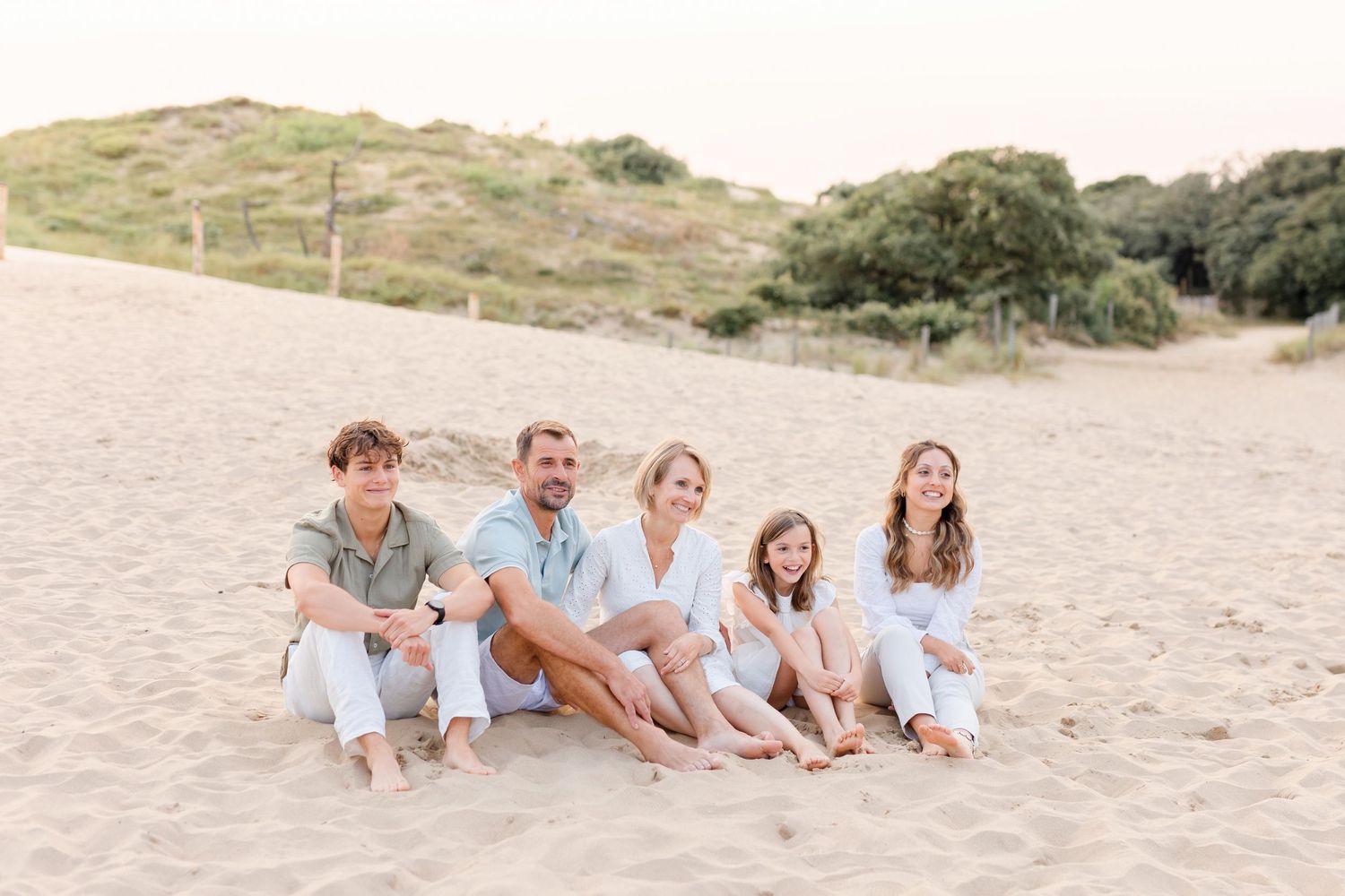 Group of people in white and neutral clothing sitting together on beach sand.