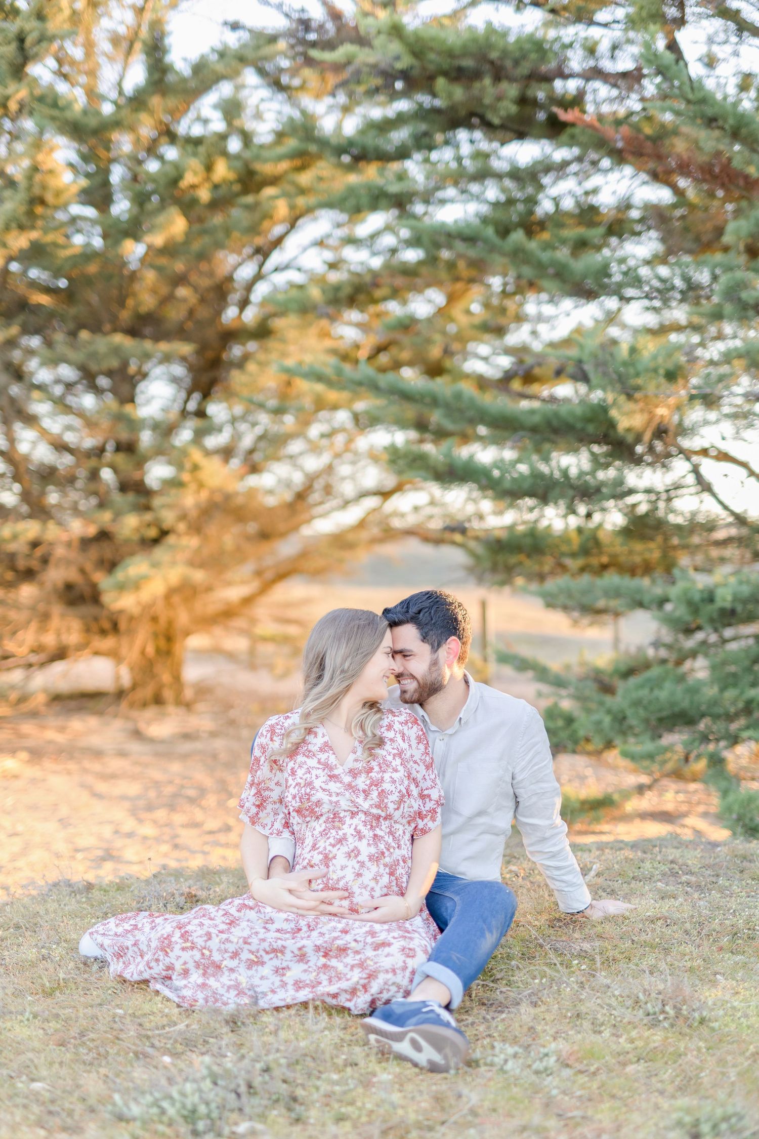 Couple sitting together under pine trees during golden hour photoshoot.