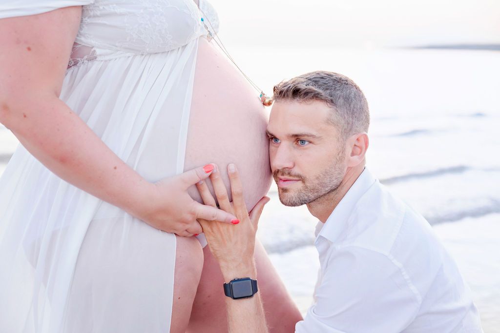 A tender moment captured during a beach maternity session at sunset.