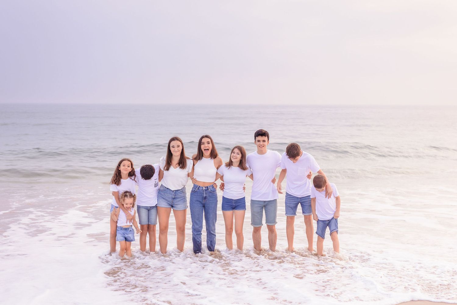 Large family group stands together at ocean's edge wearing coordinated blue and white outfits.