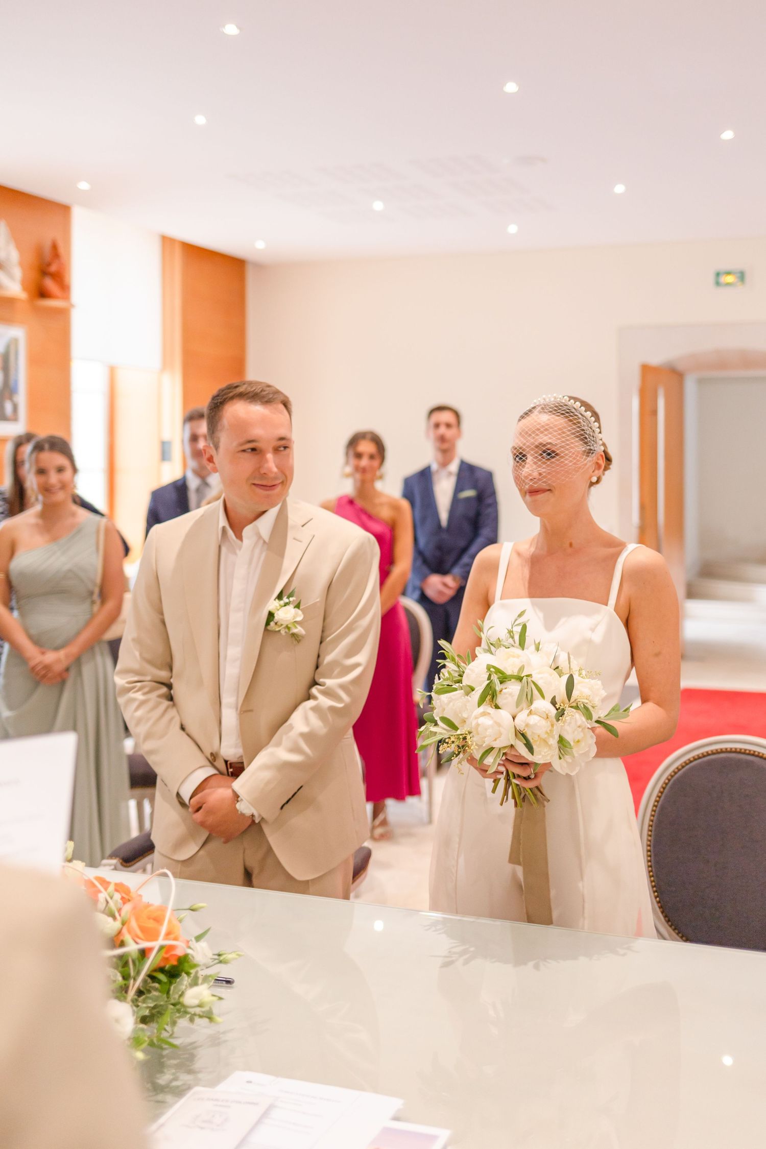 A wedding ceremony takes place in a bright indoor venue with guests watching the couple at the altar.