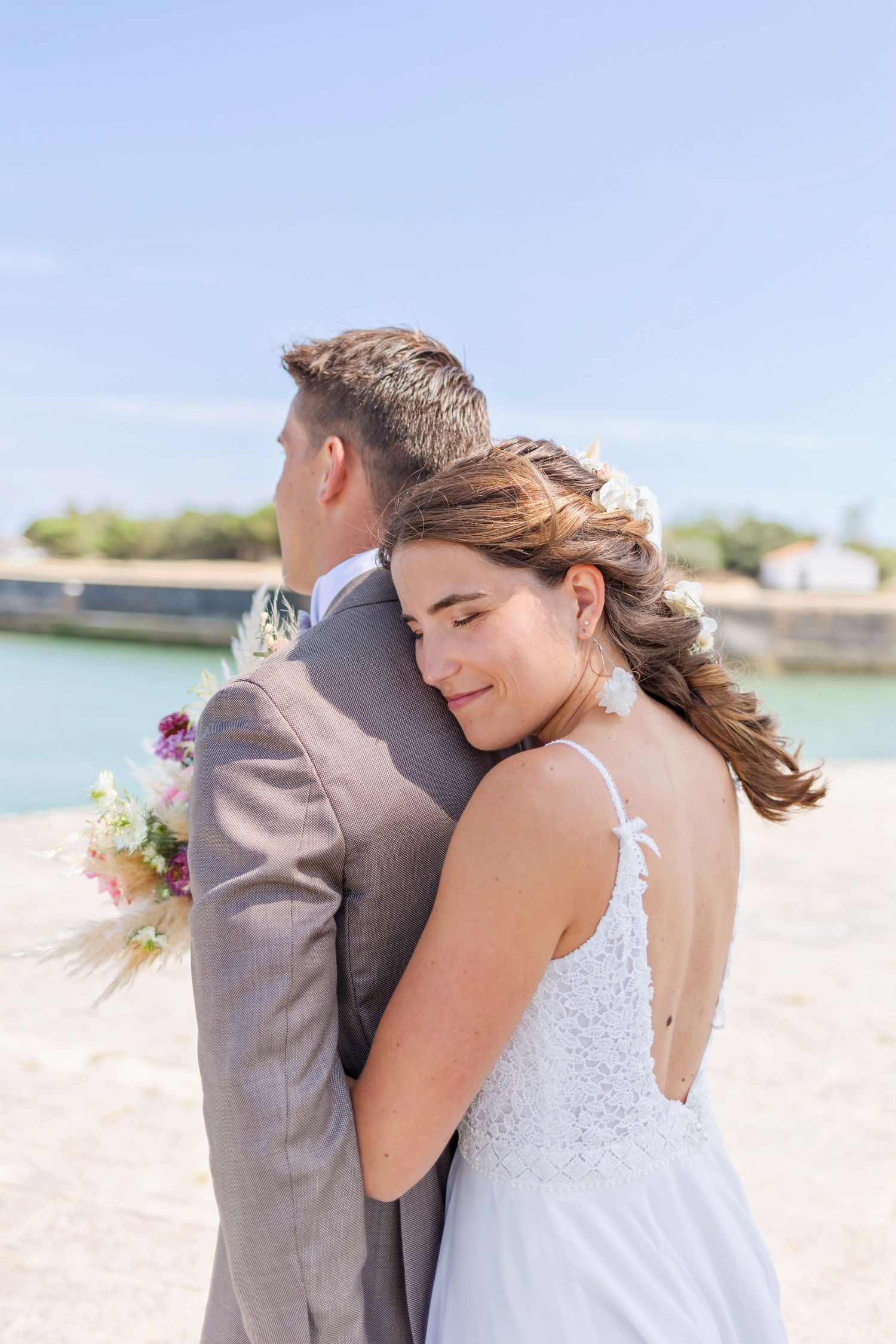 Intimate wedding portrait of couple embracing by seaside lighthouse.