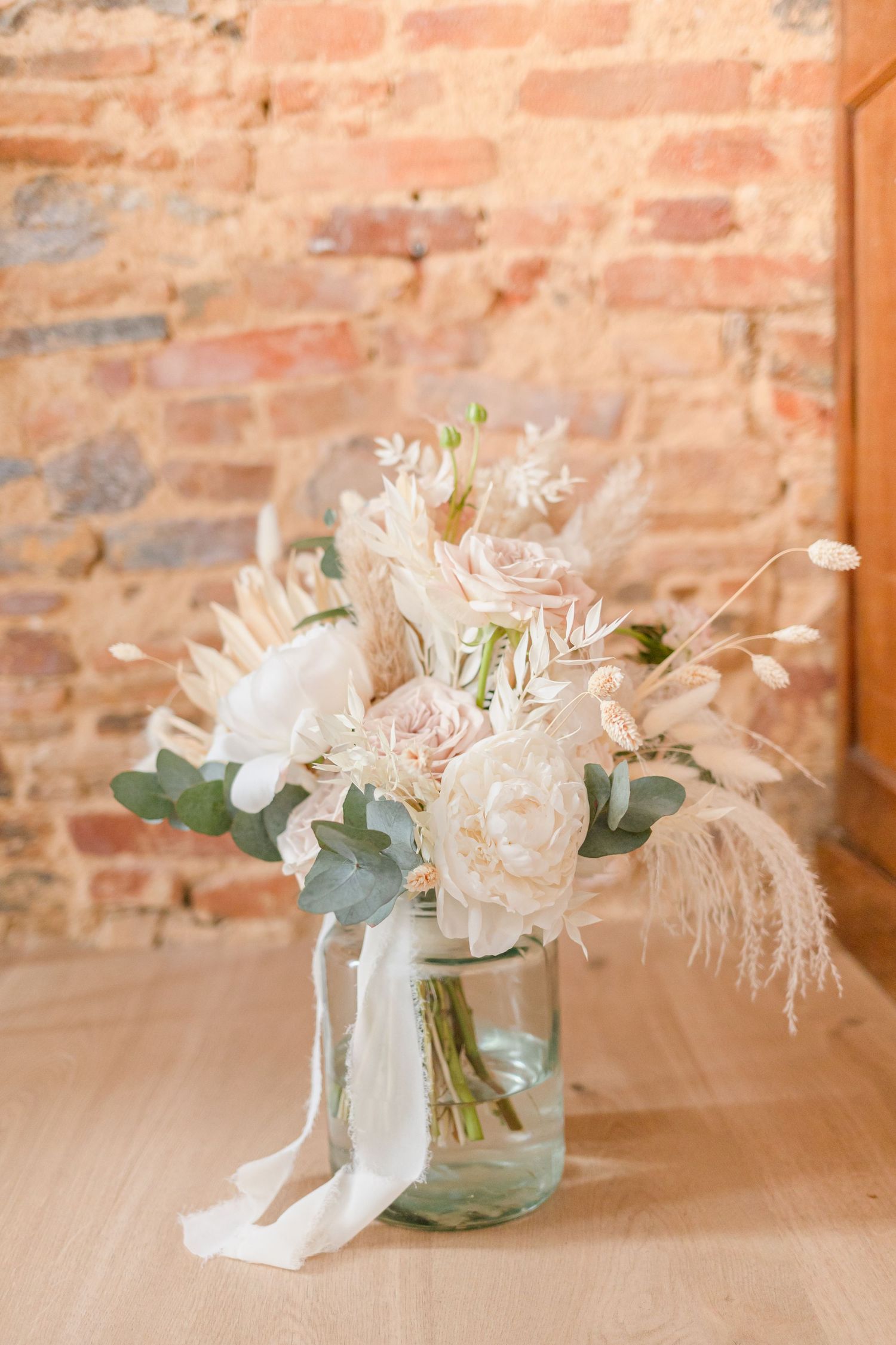 Soft pastel floral arrangement in mason jar against rustic brick wall.