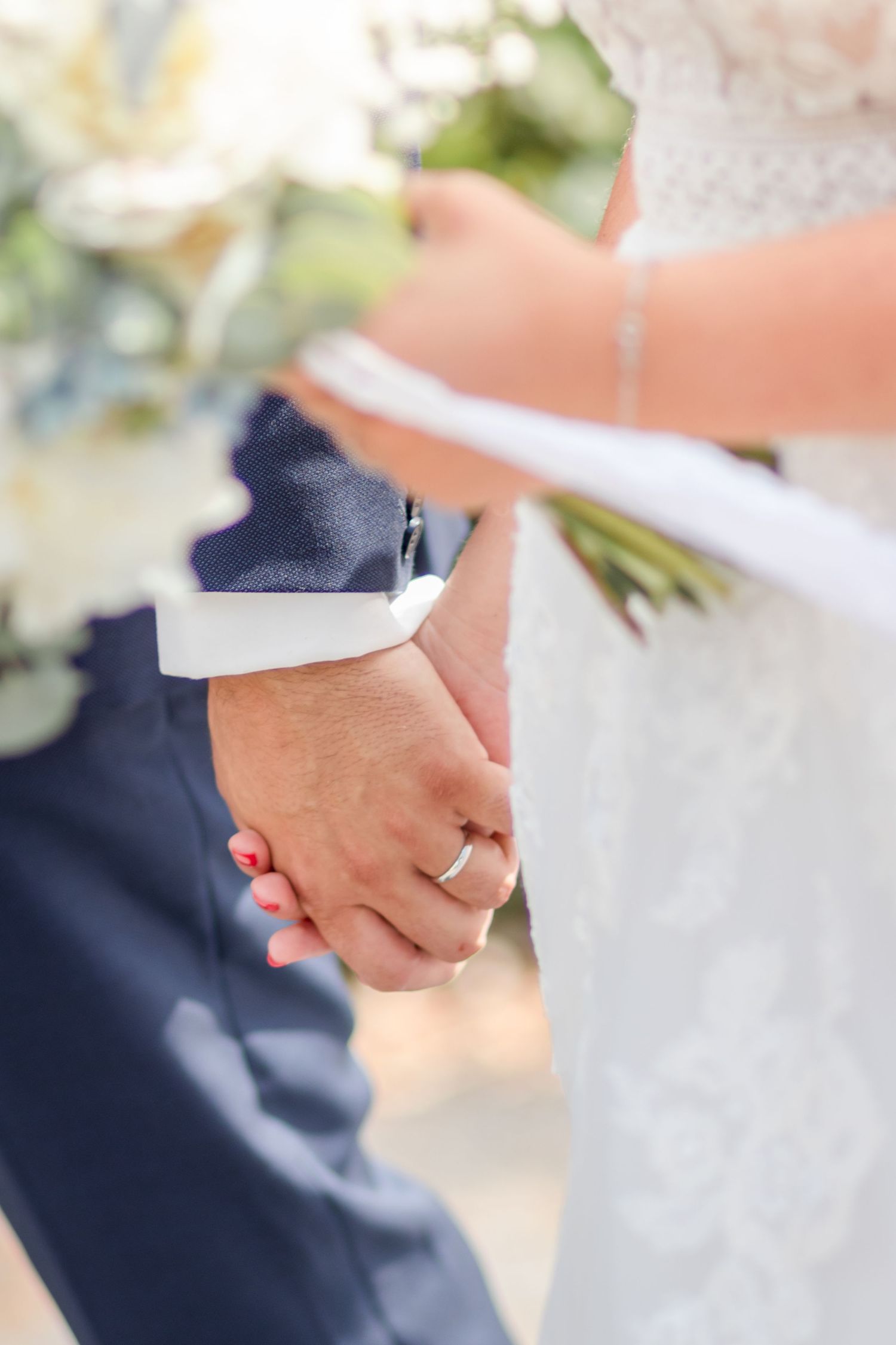 Close-up of bride and groom holding hands showing wedding rings and formal attire details.