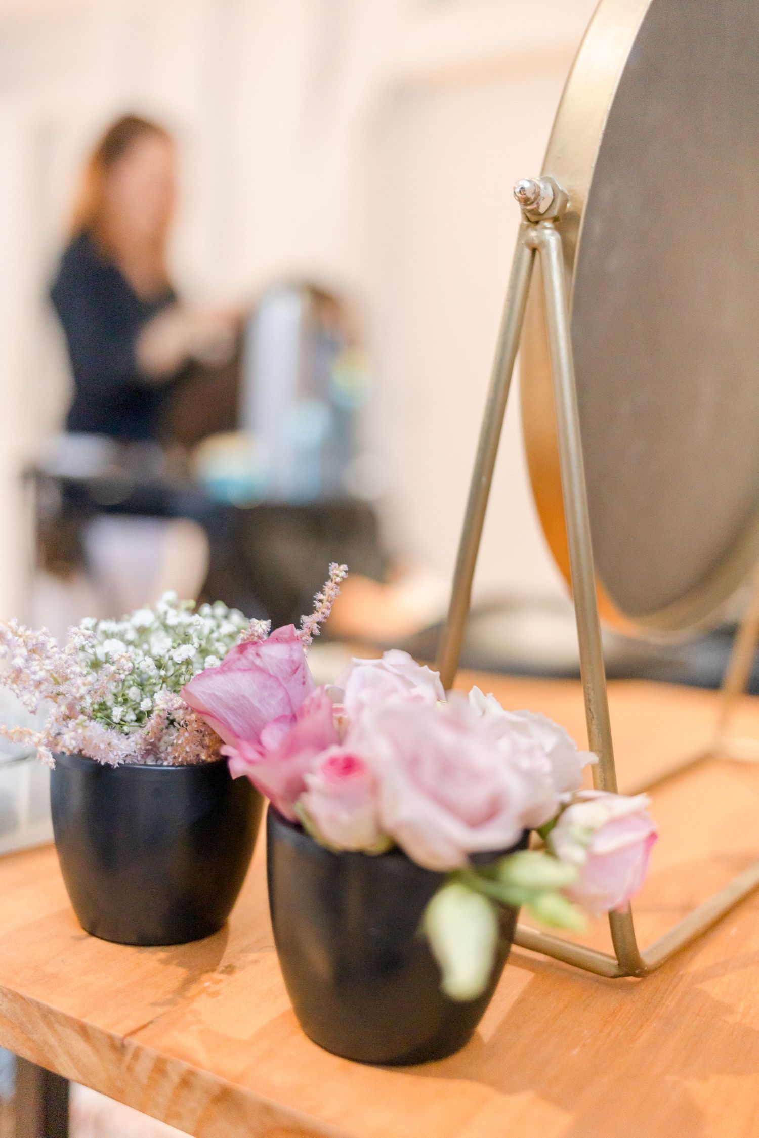 Pink roses and baby's breath in black vases next to vanity mirror.