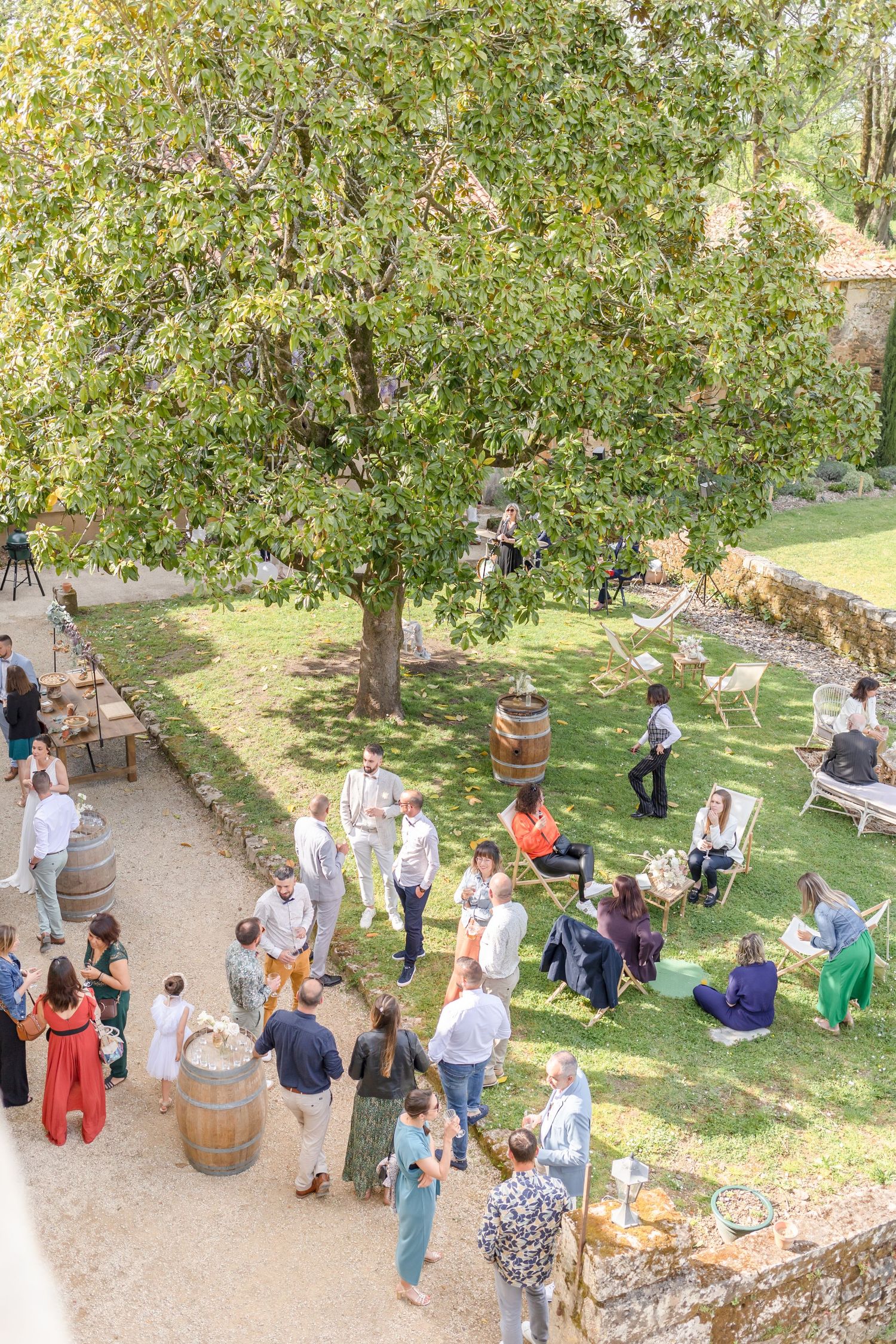 Garden party gathering with guests mingling under trees on a sunny day.