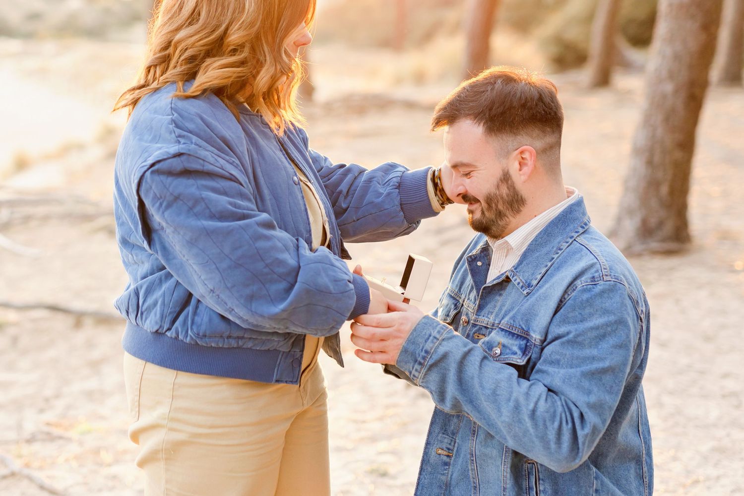 Two people wearing blue denim jackets sharing a tender moment outdoors at golden hour.