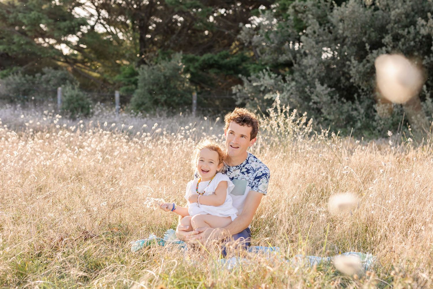 Parent and child sitting together in sunlit field with bokeh effects.