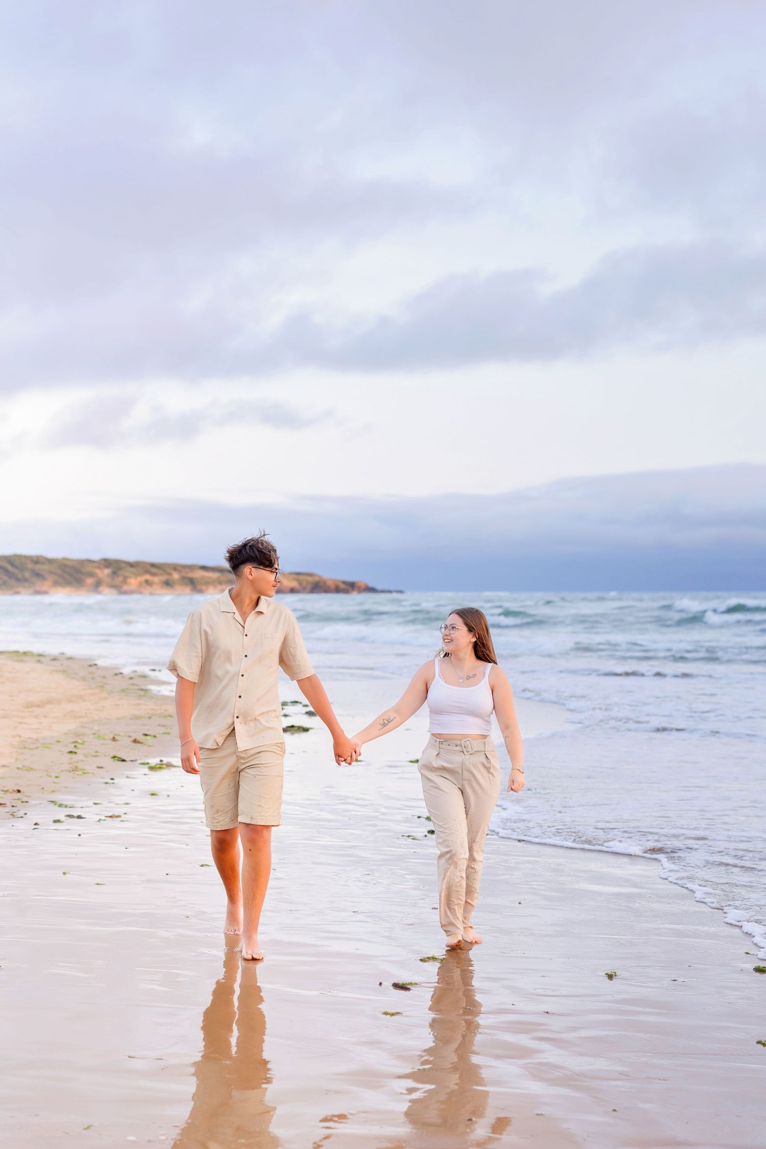 A couple holding hands while walking along the shoreline at sunset.