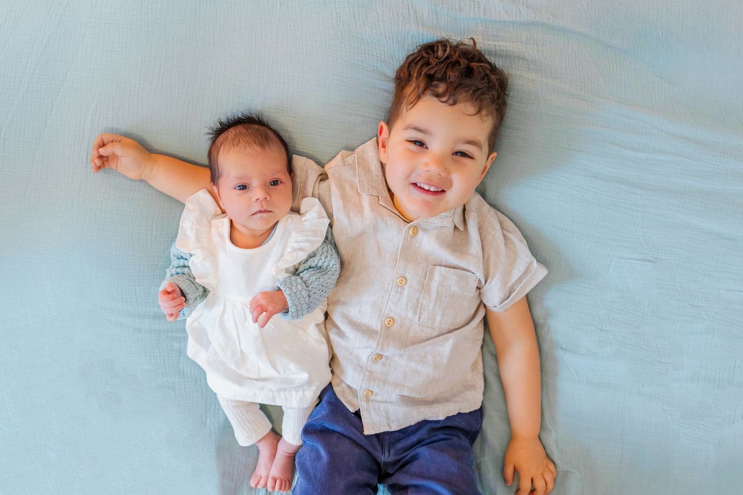Two siblings lying on light blue bedding sharing a happy moment together.