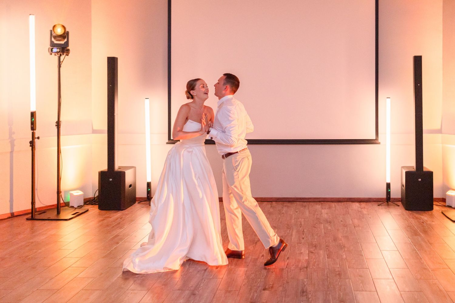 Couple dancing in elegant venue with professional lighting and projection screen backdrop.