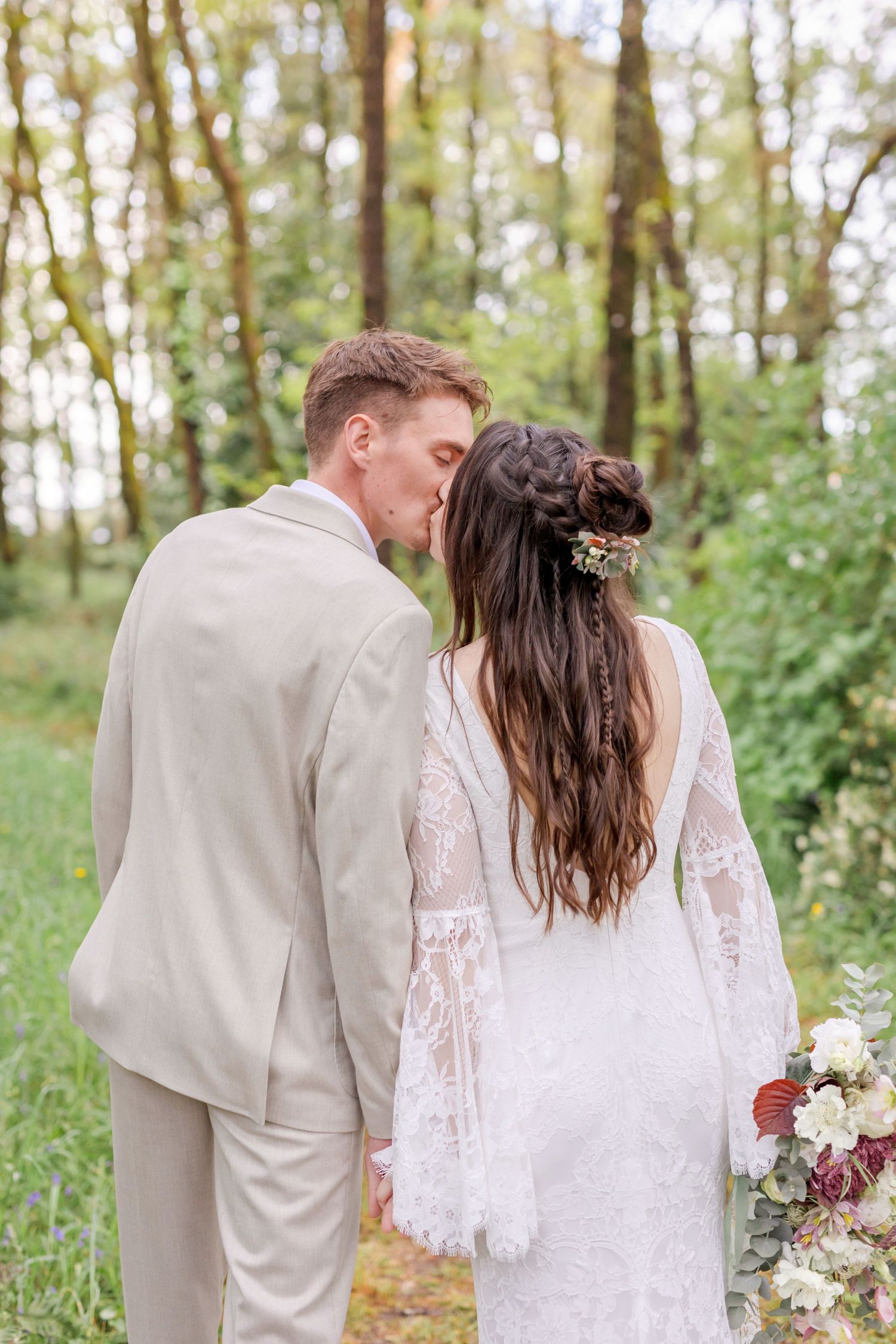 A couple in wedding attire standing close together on a forest path.