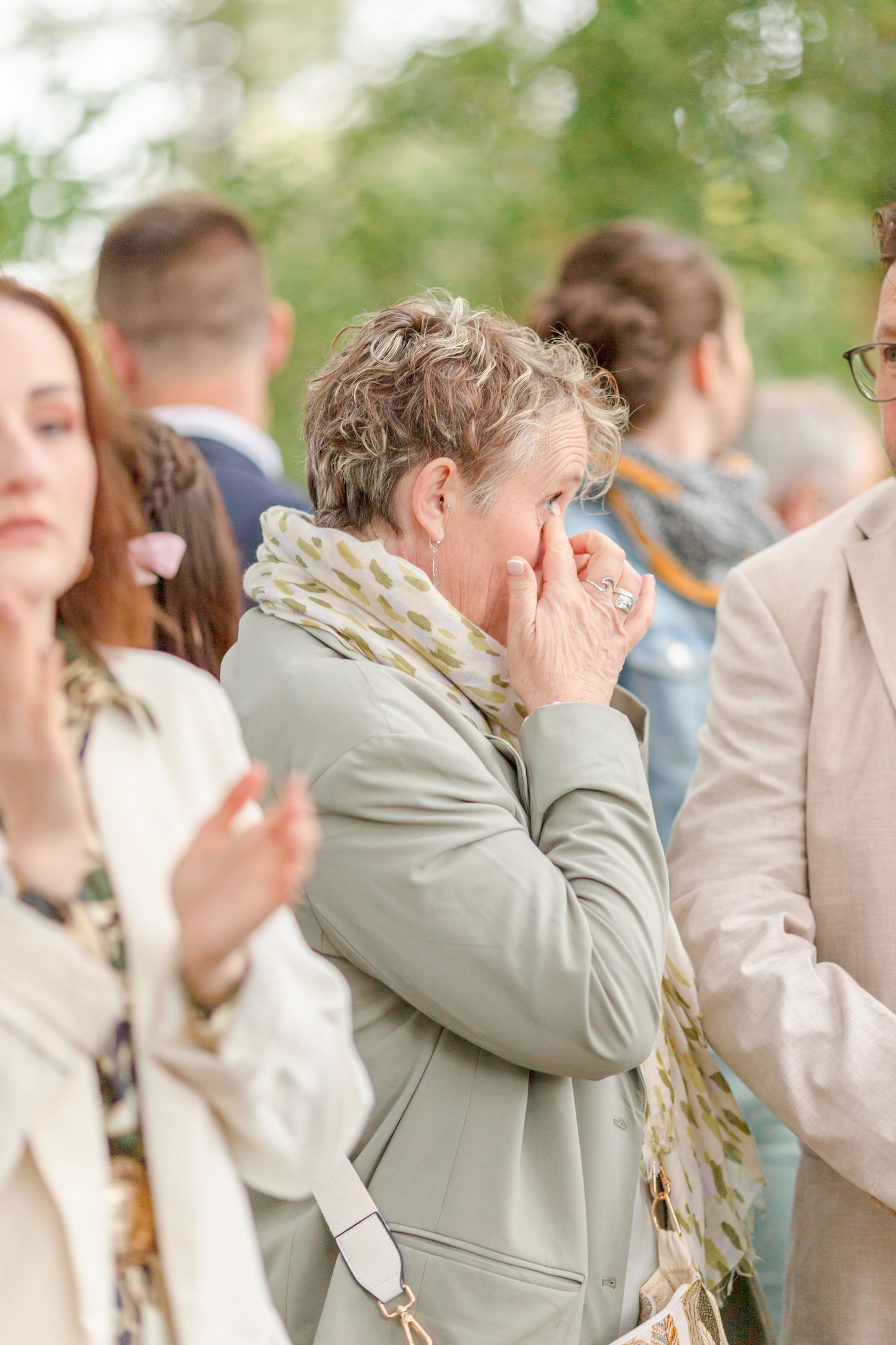 Wedding guest showing emotion during outdoor ceremony among gathered attendees.