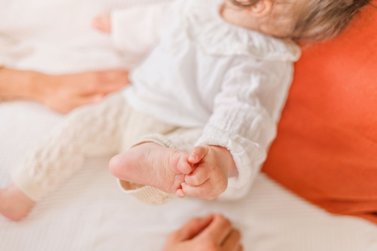 Baby's tiny hands reaching up against soft white fabric and orange accents.