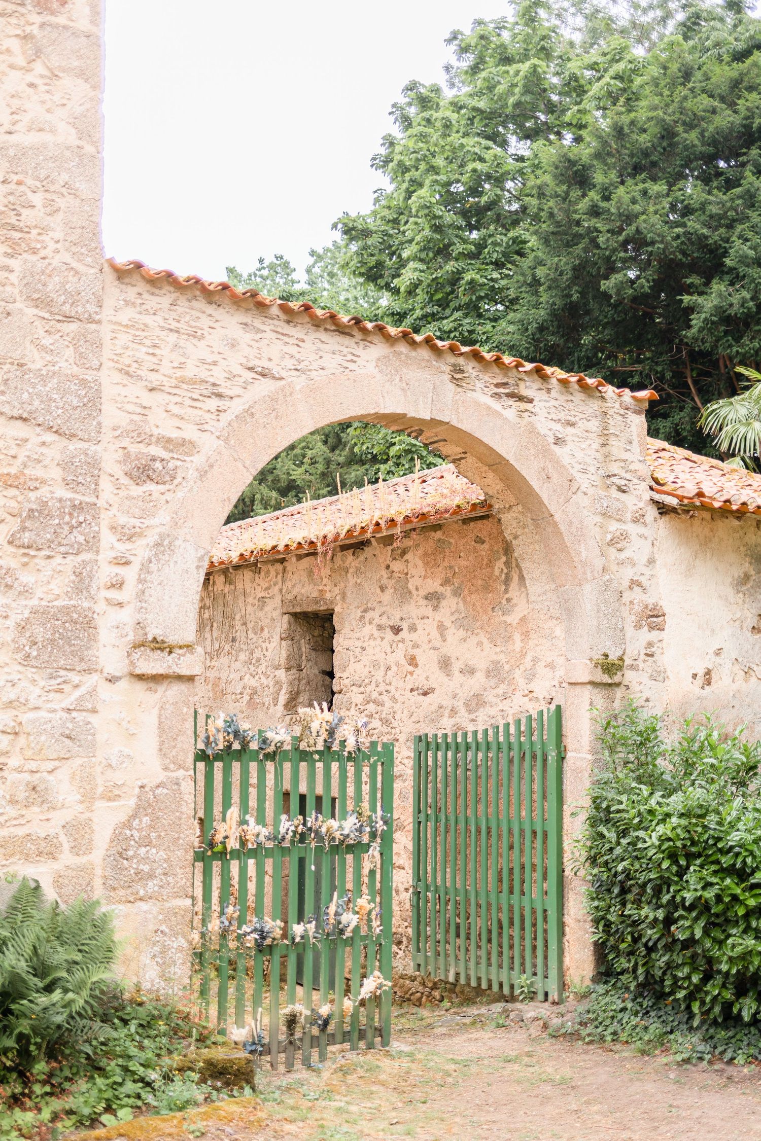 Ancient stone archway with green garden gate surrounded by lush vegetation.