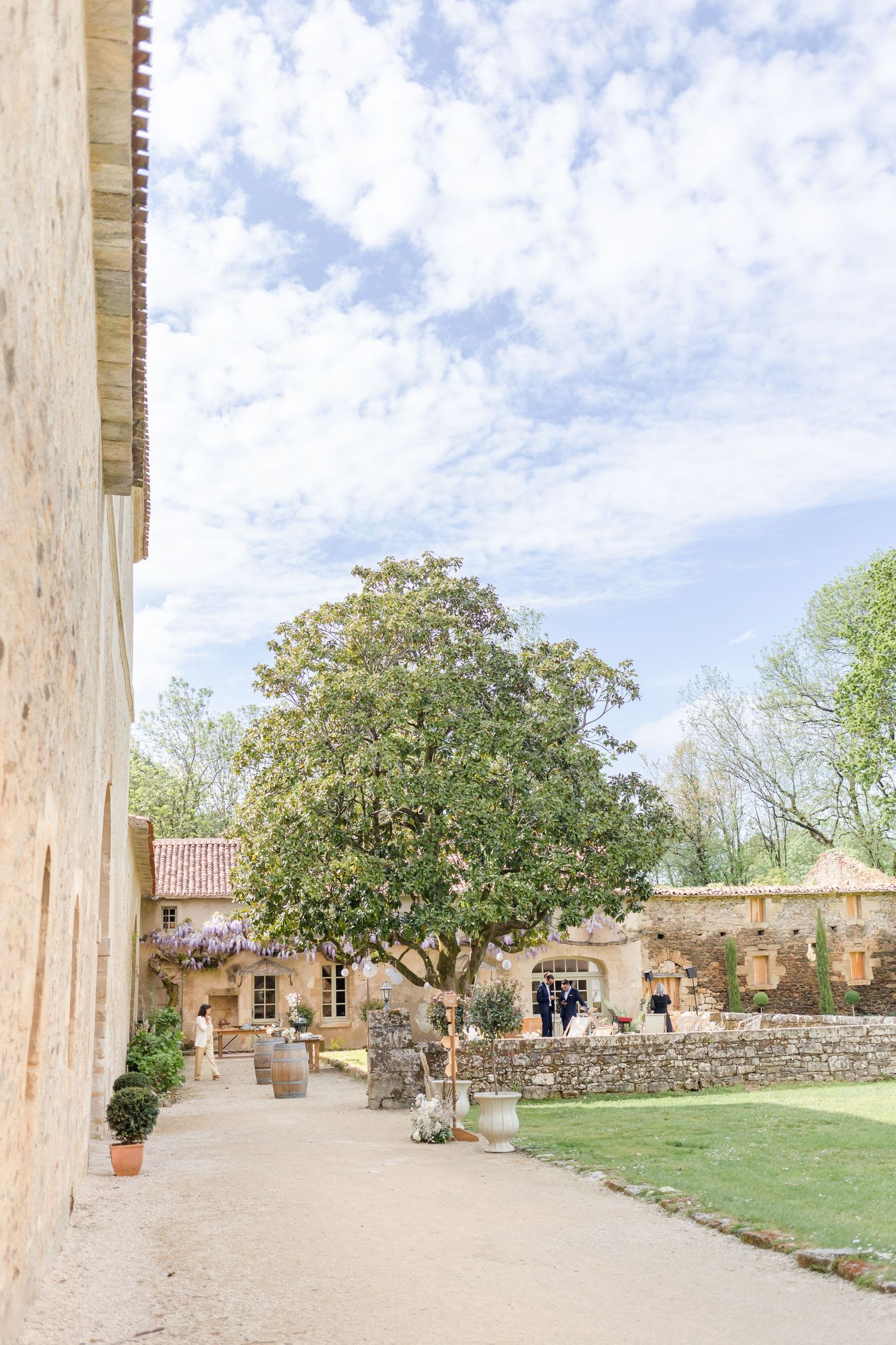 Sprawling courtyard with stone pathways surrounded by manicured lawns and mature trees under blue skies.