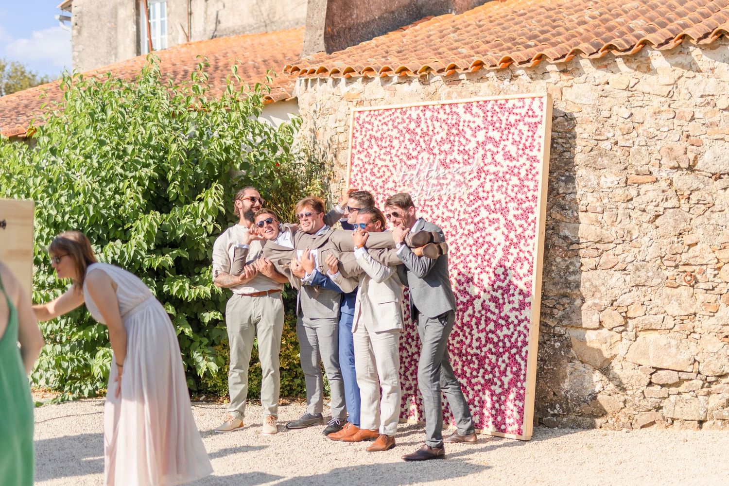 Wedding party guests gather outside a rustic stone building in an outdoor celebration.