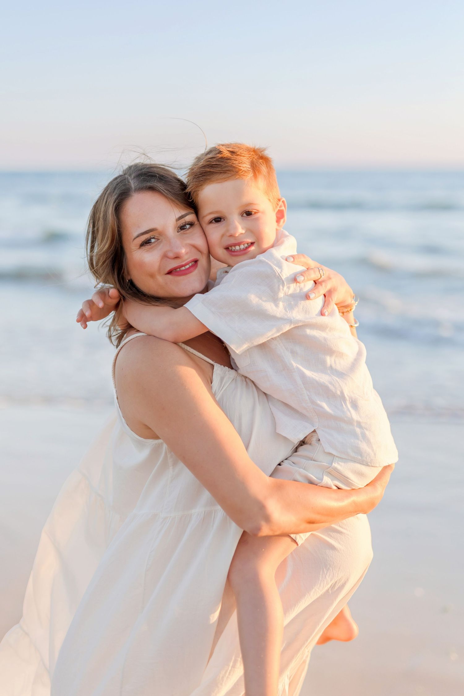 Joyful beach portrait featuring embracing figures in white against ocean backdrop.