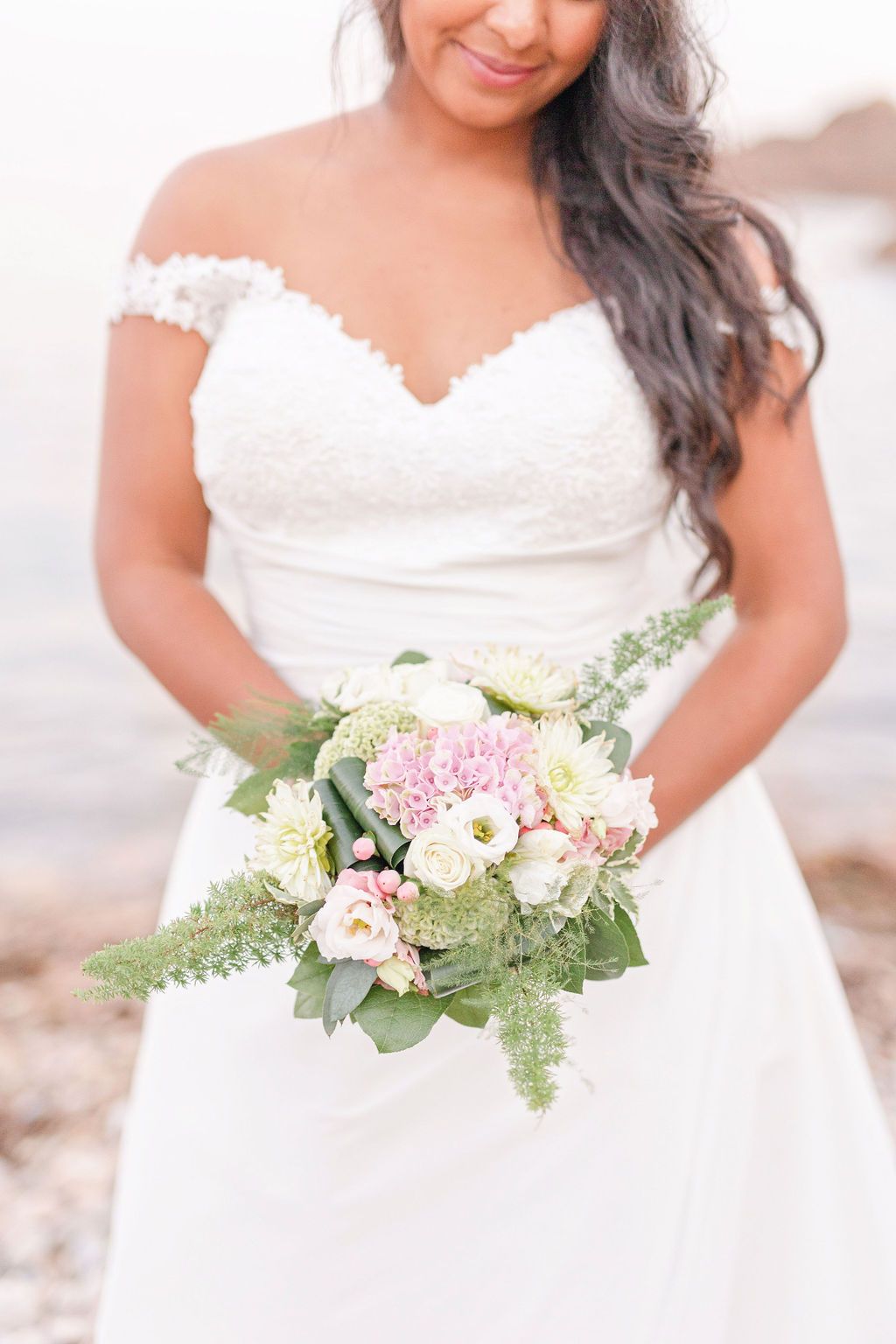 A bride in a white lace dress holds a beautiful bouquet of pink and white flowers.