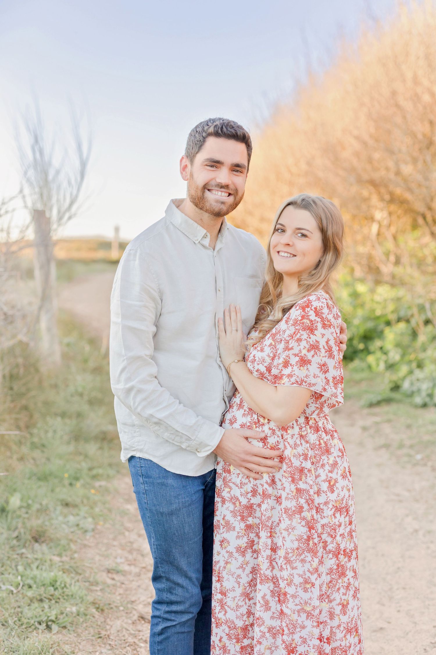 A couple sharing an intimate moment on a sunlit path with fall colors in the background.