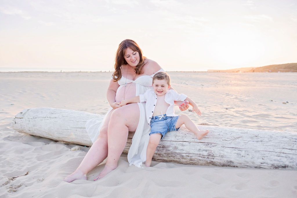 Mother and child share a moment while sitting on driftwood at the beach.