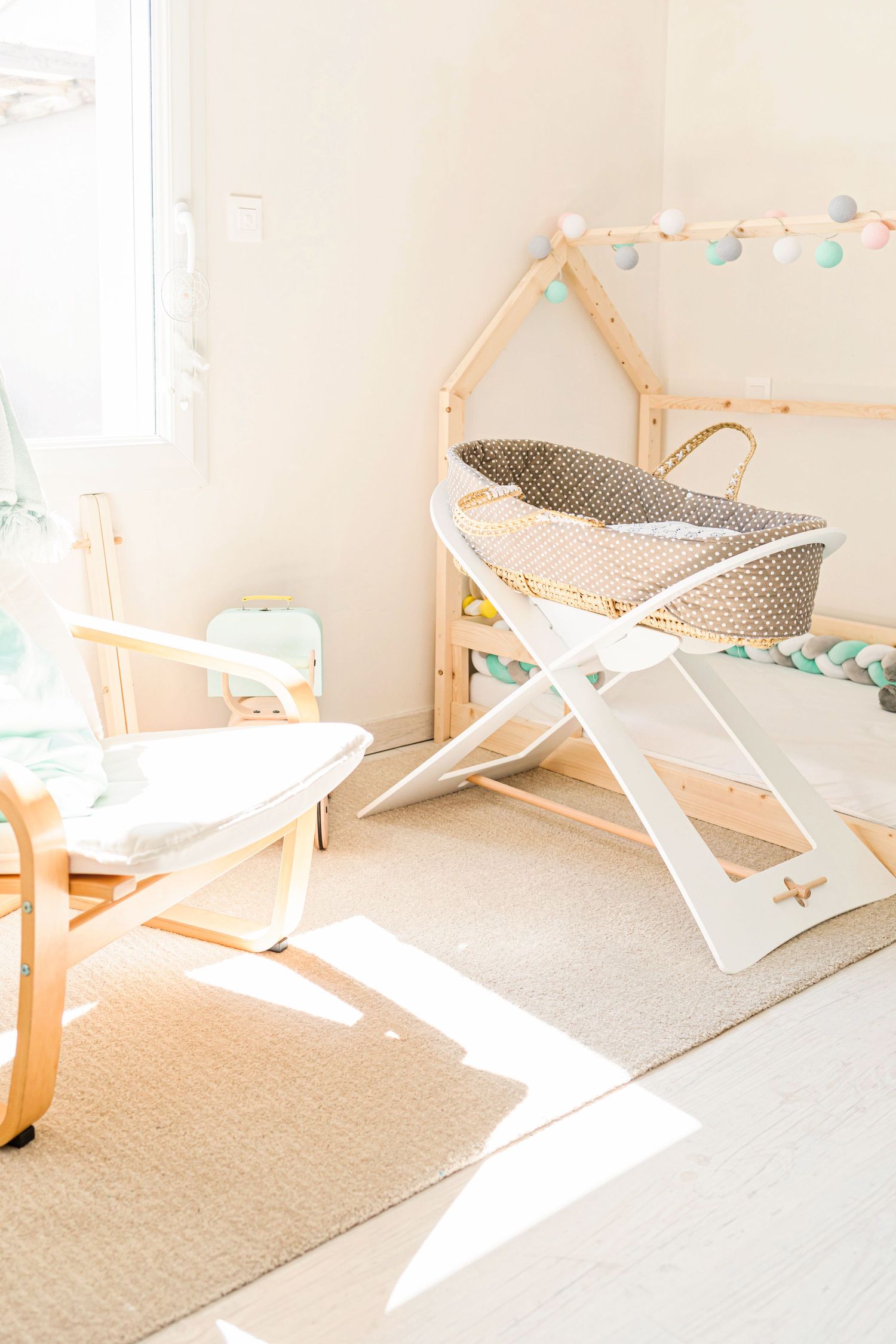 Nursery room with wooden bassinet, string lights, and natural sunlight streaming through window.