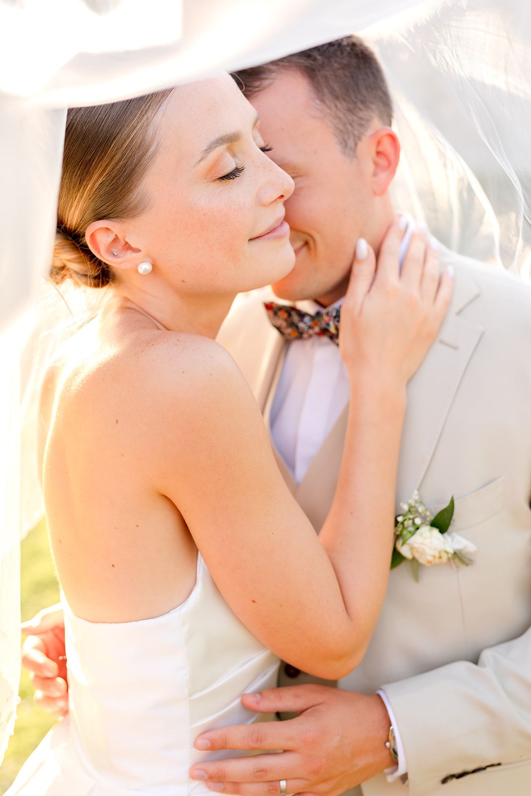 Cropped shot showing elegant wedding attire with white dress and tan vest with bow tie.