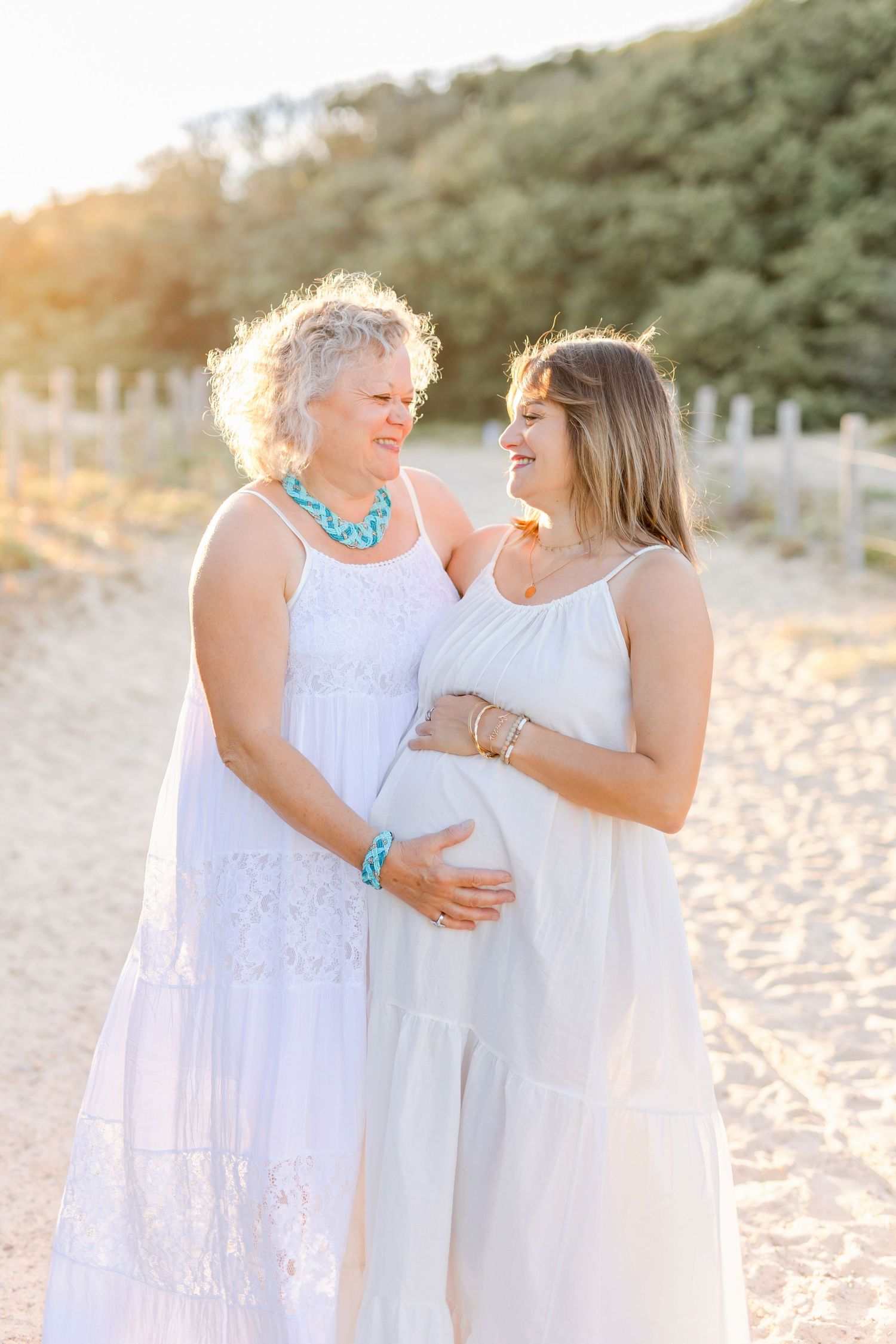 Two people in white dresses embrace on a sandy beach during golden hour.