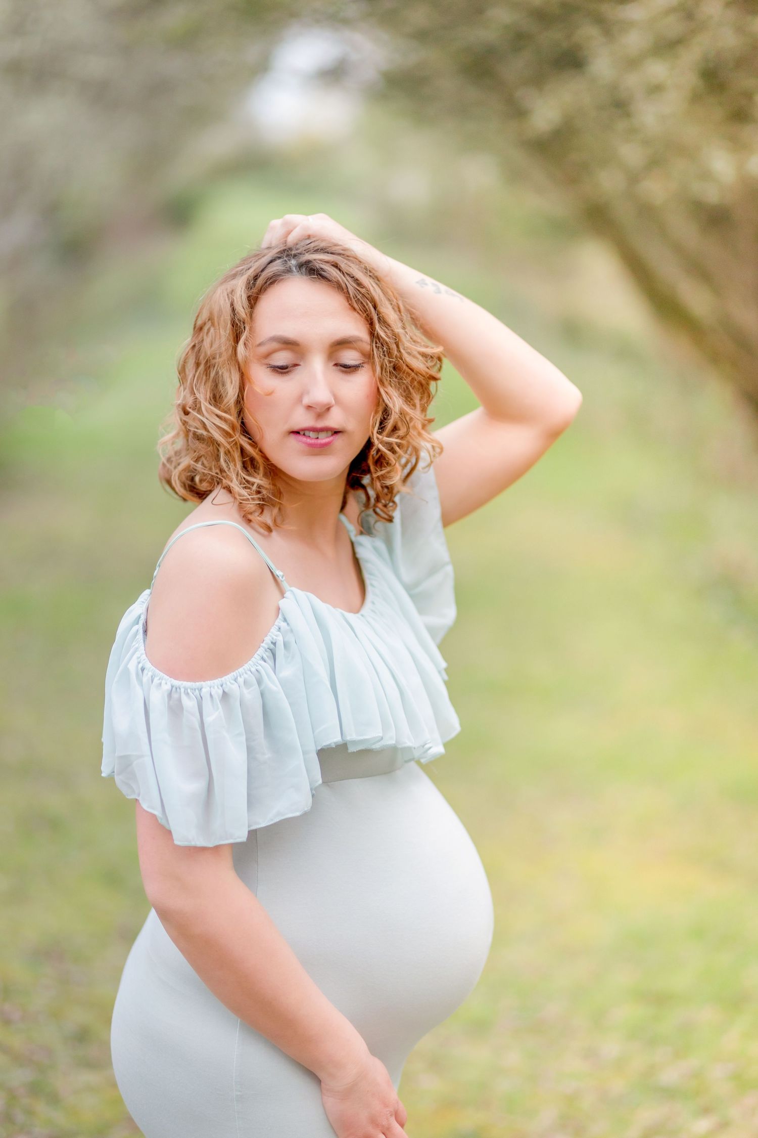 Ethereal maternity portrait in a white ruffled dress amidst a soft, natural outdoor setting.