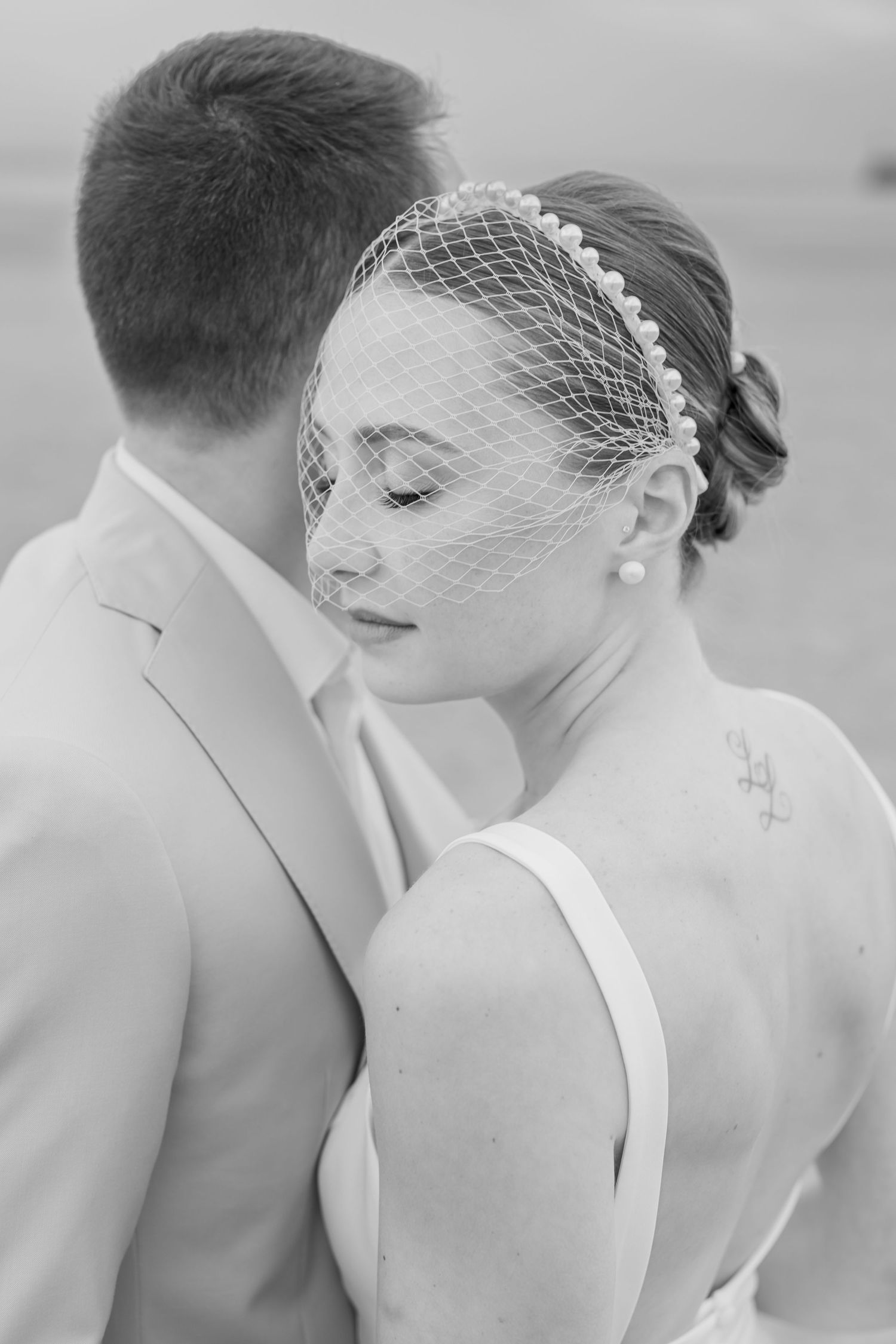 A close-up black and white shot of a bride wearing a birdcage veil headpiece.