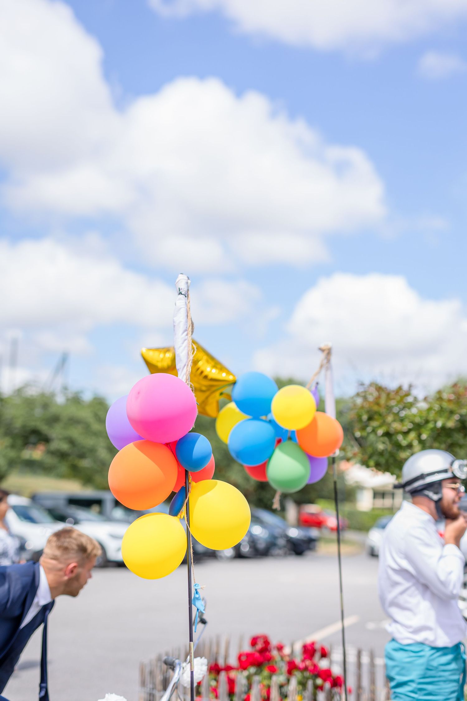 Colorful balloons float against blue sky at outdoor wedding celebration.