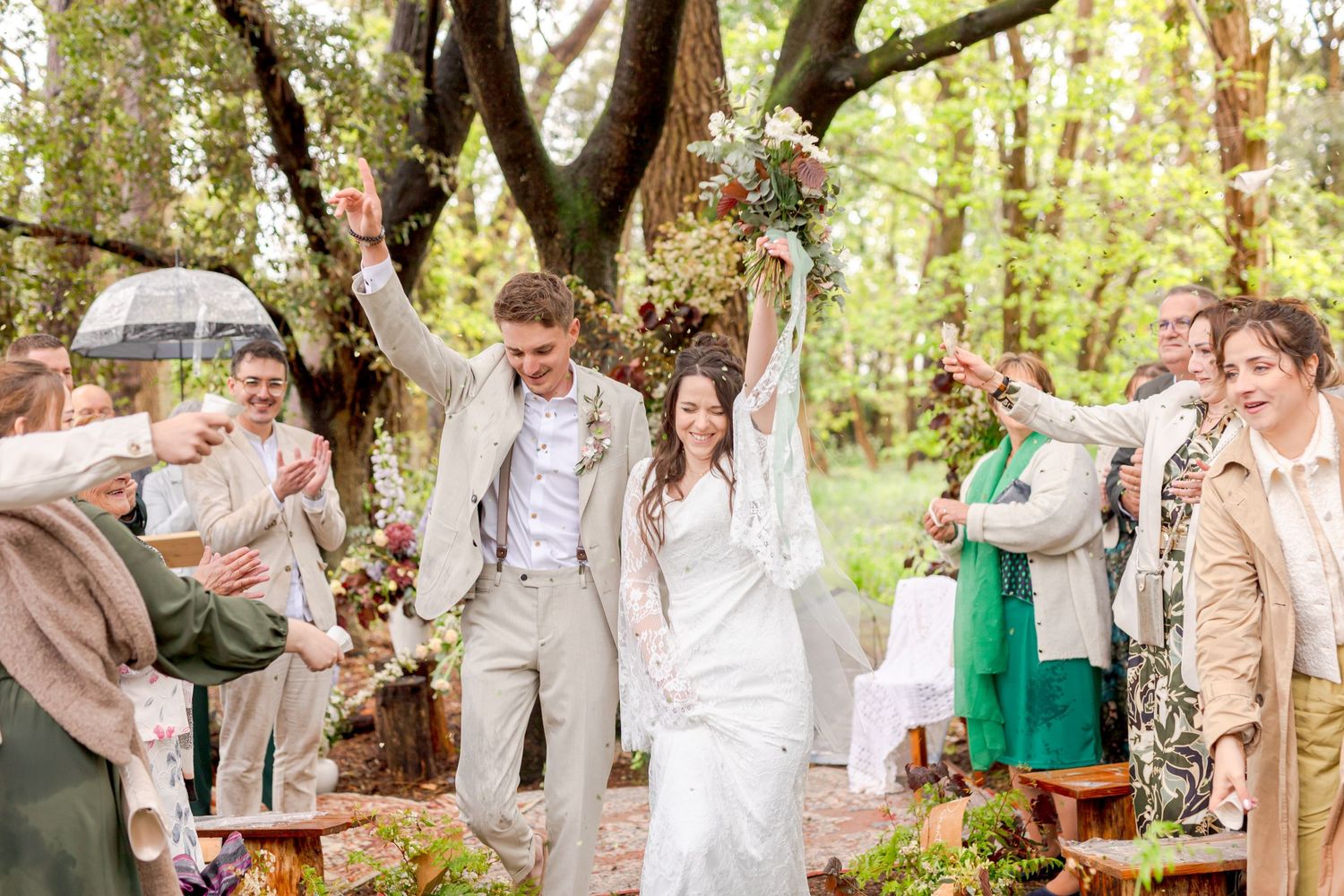 Wedding guests cheer as the newlyweds celebrate at a forest ceremony.