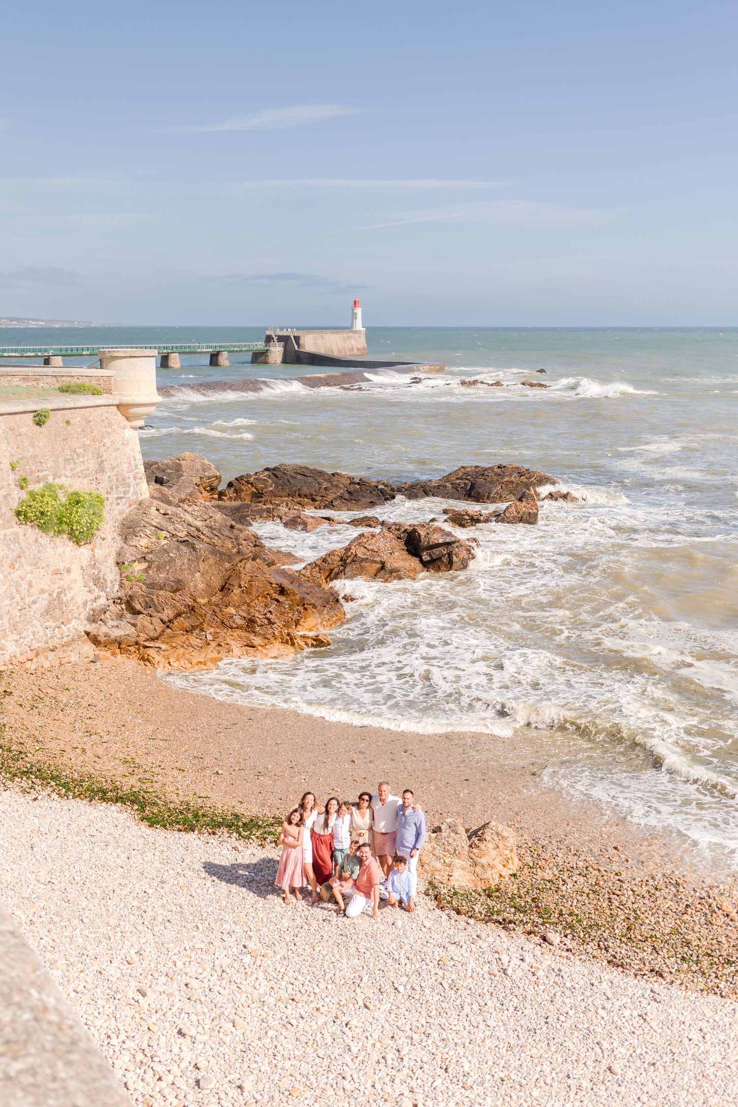 Family enjoying seaside view from rocky beach near historic stone fortress and lighthouse.