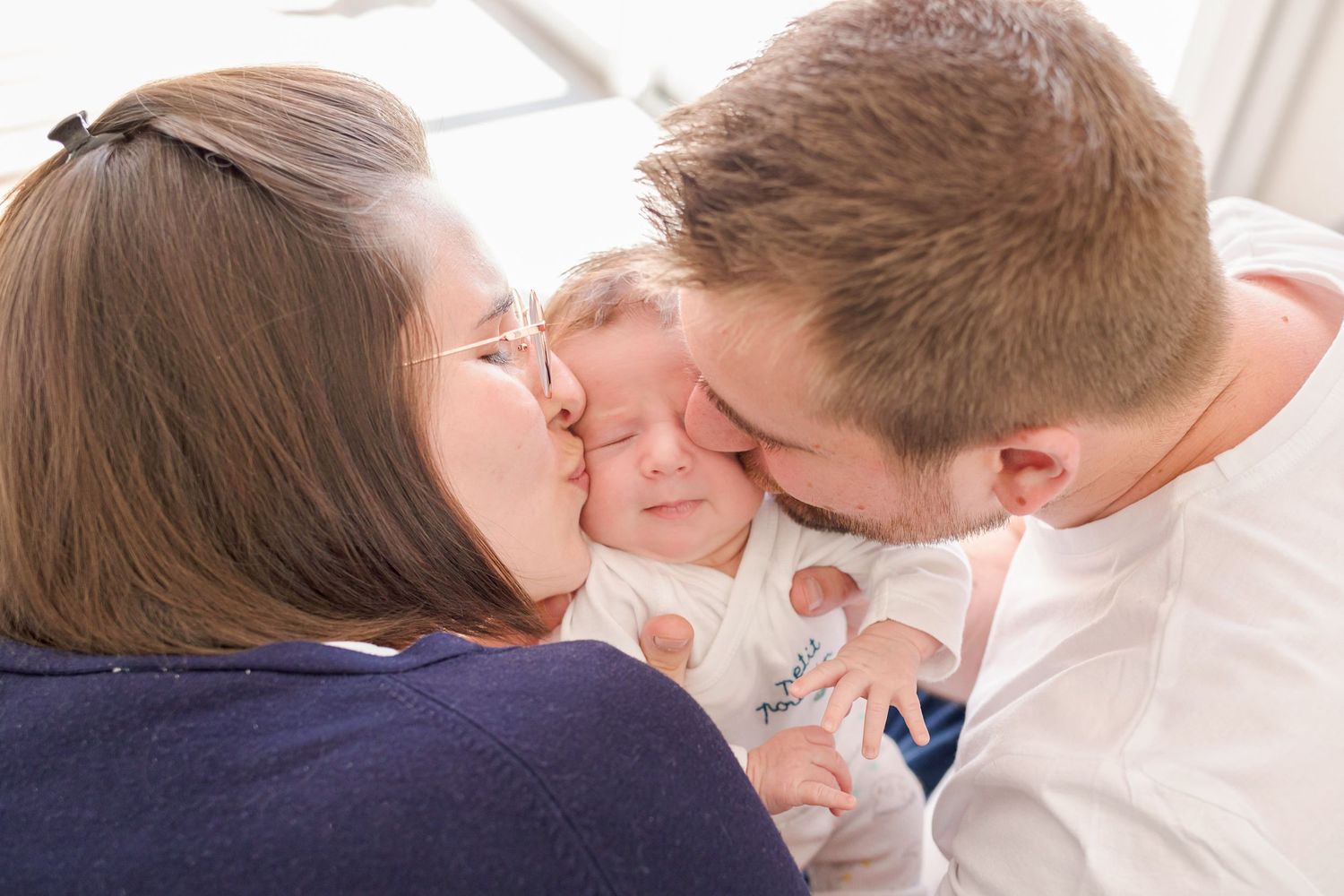 Sweet family moment showing affection to an infant in white clothing.