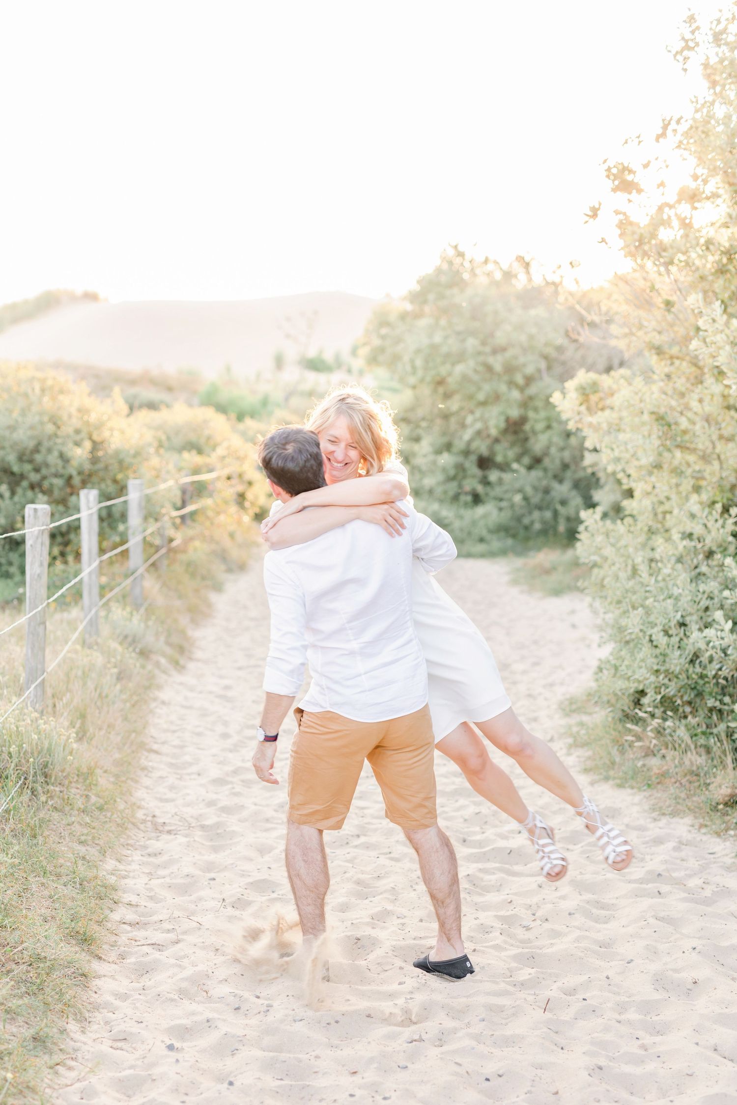 Dancing couple spins joyfully on a sandy beach path at sunset.