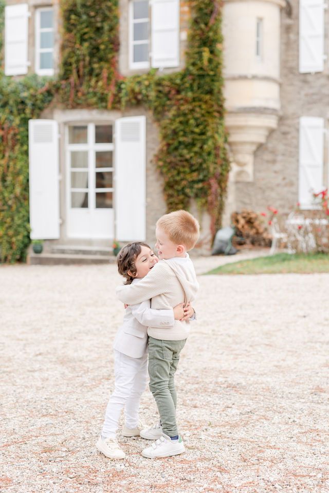 Two young children embrace while playing outside a historic stone mansion.
